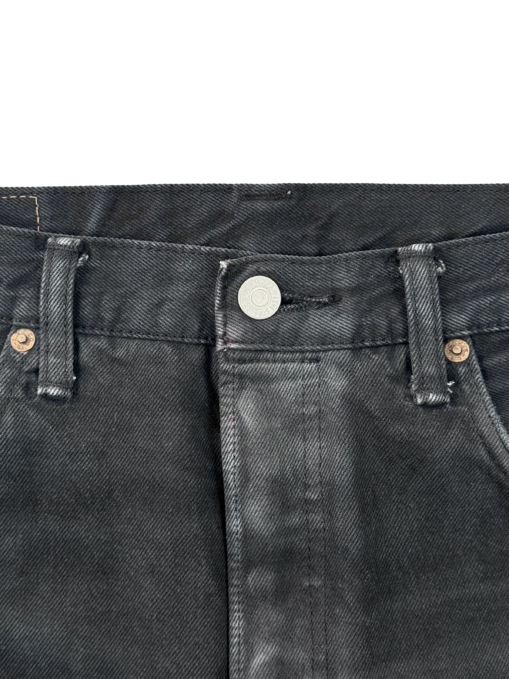 Fokus auf den silbernen Verschlussknopf der Levi's 501 mit deutlichen Abnutzungsspuren am umliegenden Stoff.