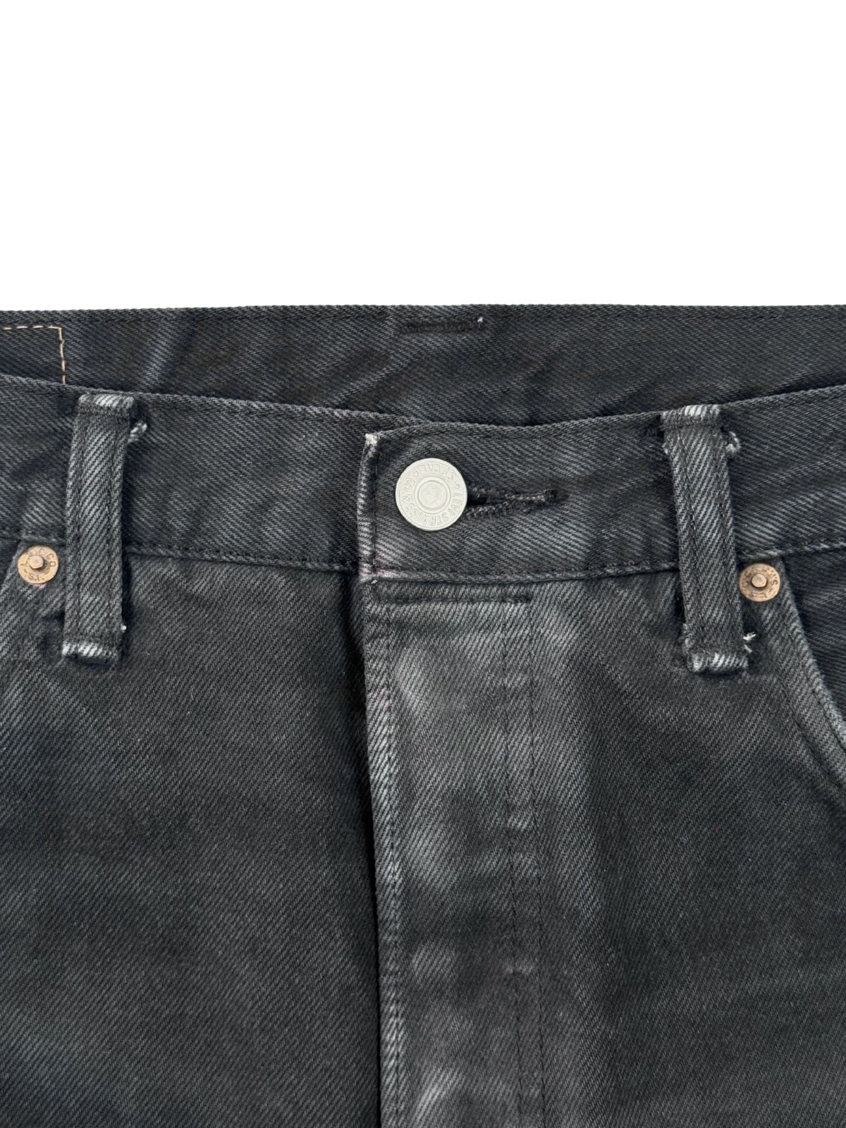 Fokus auf den silbernen Verschlussknopf der Levi's 501 mit deutlichen Abnutzungsspuren am umliegenden Stoff.