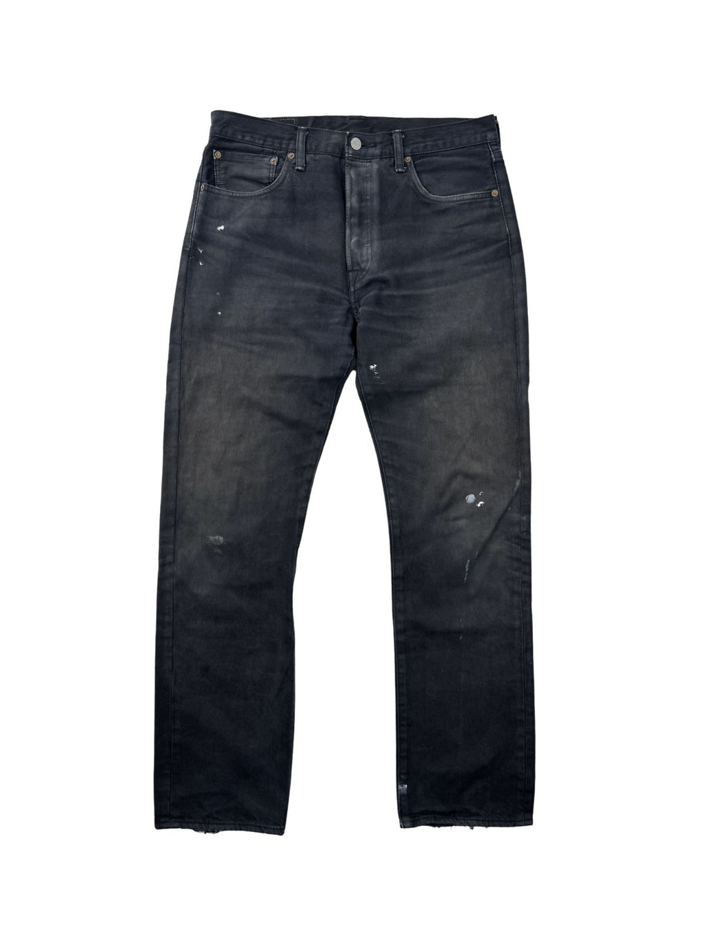 Vorderseite einer schwarz gefärbten Vintage Levi's 501 Jeans; zeigt ungleichmäßiges Fading und weiße Farbspritzer (Paint Splatter) auf dunklem Denim.