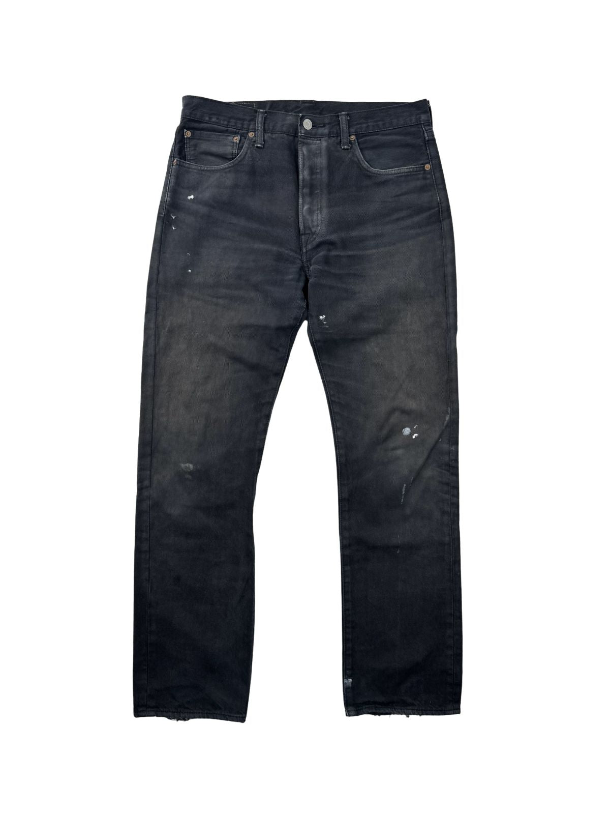 Vorderseite einer schwarz gefärbten Vintage Levi's 501 Jeans; zeigt ungleichmäßiges Fading und weiße Farbspritzer (Paint Splatter) auf dunklem Denim.