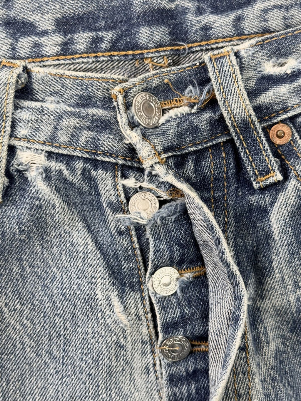 Fokus auf die Knopfleiste der Levi's 501; zeigt die geprägten Metallknöpfe und die distressed Struktur des Denim-Verschlusses.