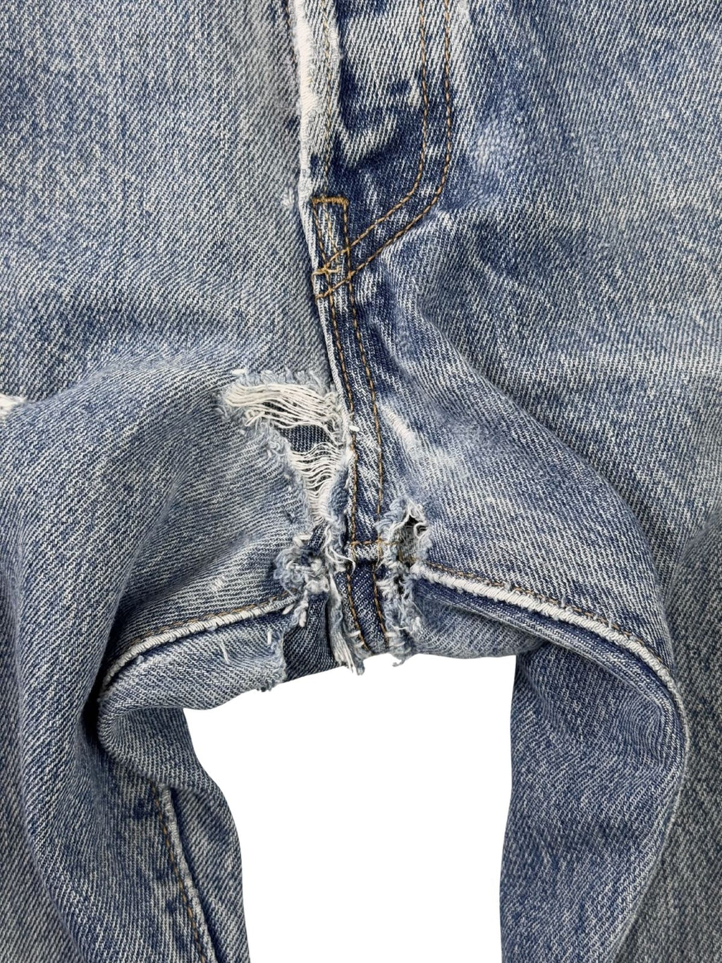 Detailaufnahme einer handgenähten Reparatur im Schrittbereich (Crotch) der Jeans; zeigt dunkle, kreuzförmige Sticknähte auf dem hellblauen Denim im Boro-Stil.