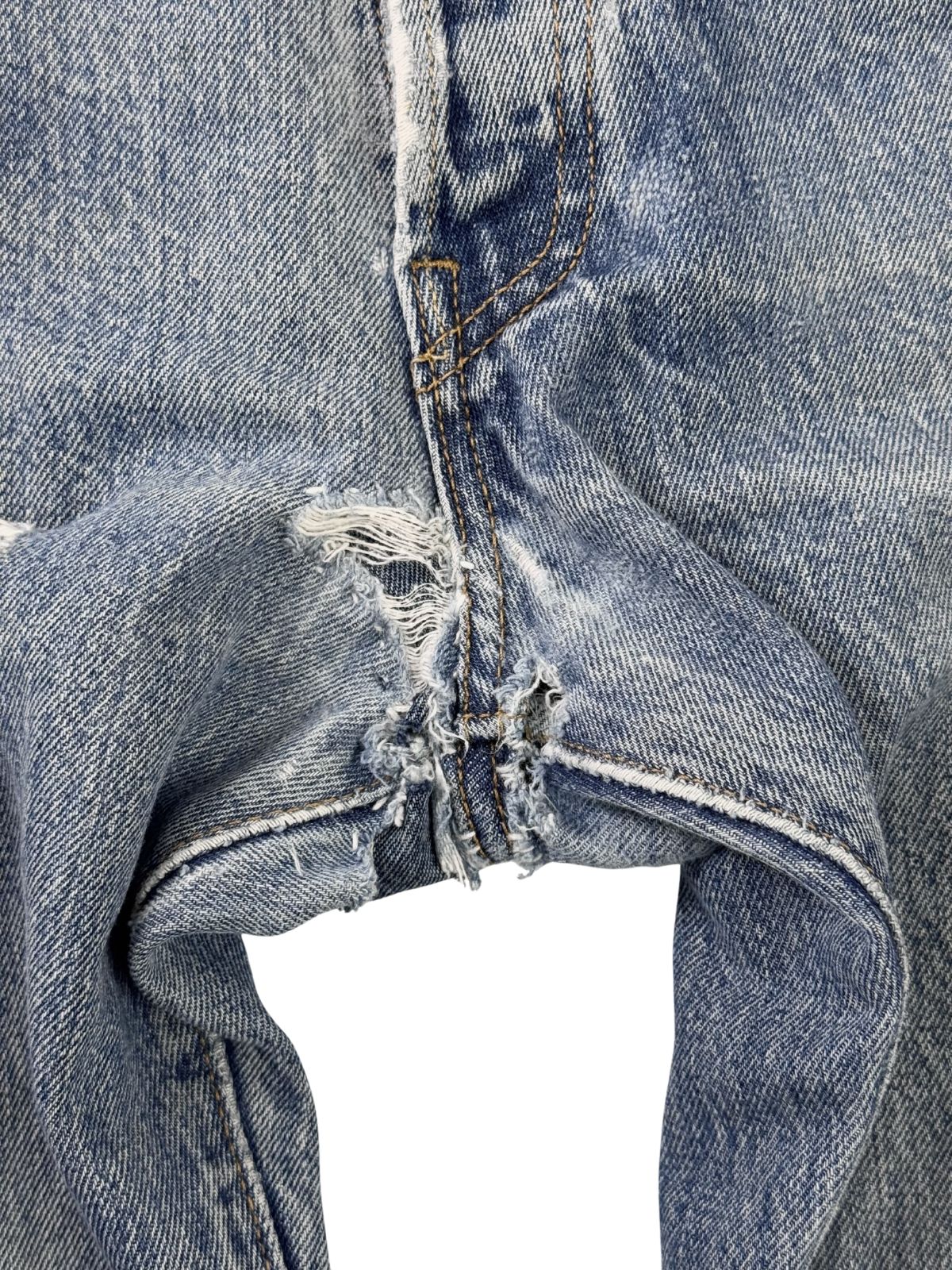 Detailaufnahme einer handgenähten Reparatur im Schrittbereich (Crotch) der Jeans; zeigt dunkle, kreuzförmige Sticknähte auf dem hellblauen Denim im Boro-Stil.