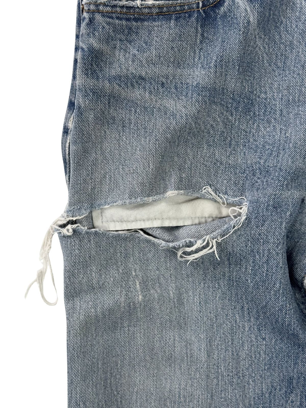 Nahaufnahme eines großen Risses am Oberschenkel; zeigt die freigelegten weißen Schussfäden und die stark strukturierte Oberfläche des gealterten Vintage-Denims.