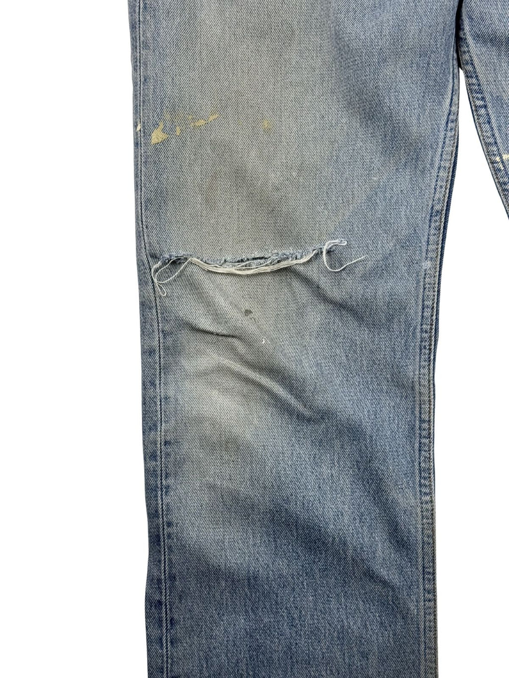 Detailansicht des rechten Knies mit einem großen, offenen Riss im Denim, leichten gelblichen Flecken und authentischem Vintage-Abnutzungscharakter.