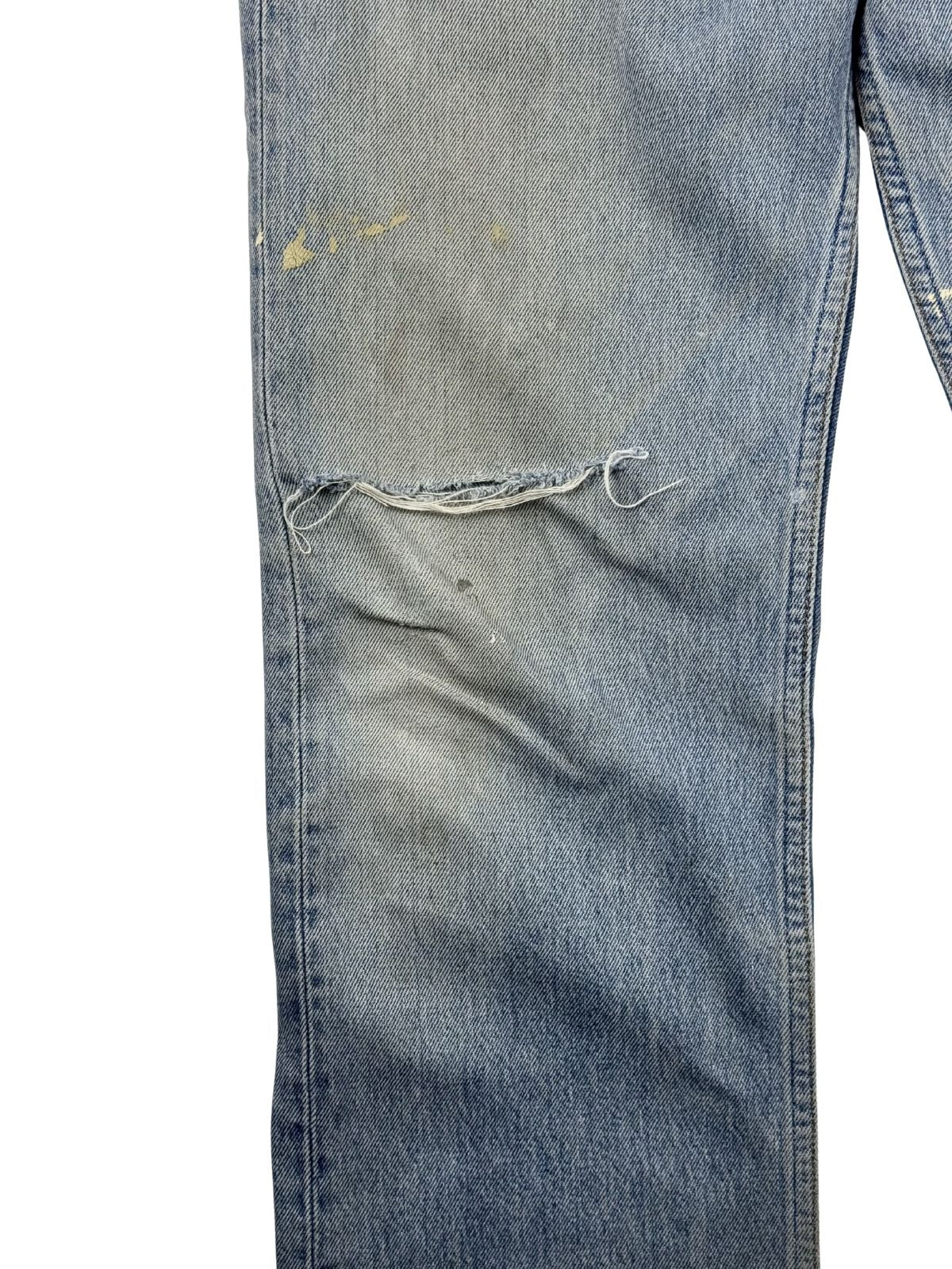 Detailansicht des rechten Knies mit einem großen, offenen Riss im Denim, leichten gelblichen Flecken und authentischem Vintage-Abnutzungscharakter.
