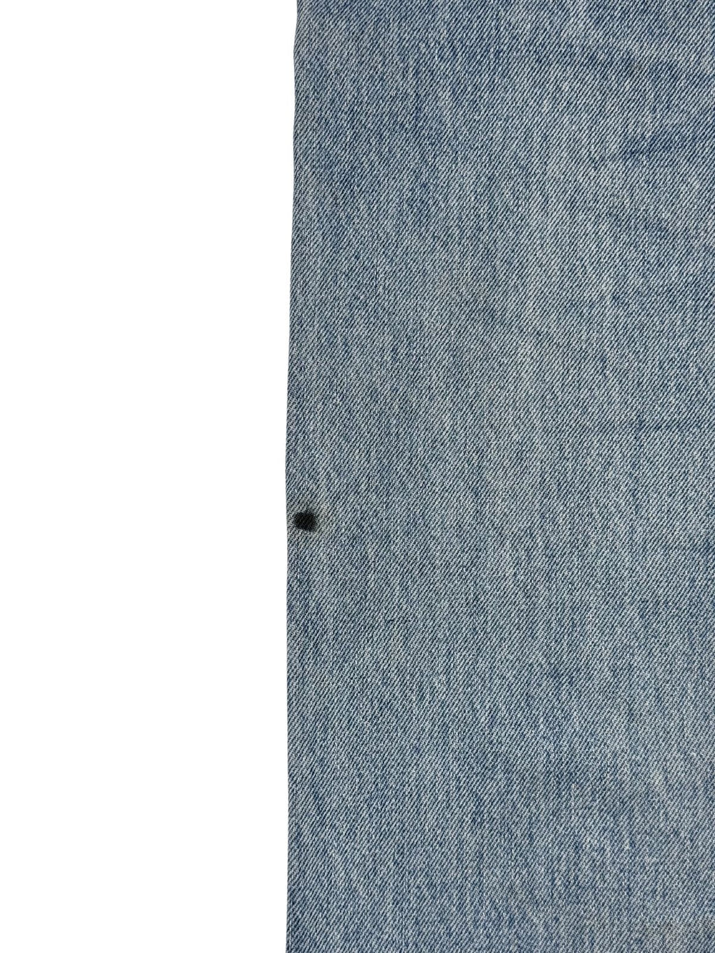 Makroaufnahme eines kleinen, tiefschwarzen Farbflecks auf dem hellblauen Jeansstoff zur transparenten Dokumentation von Mängeln im Vintage-Shop.