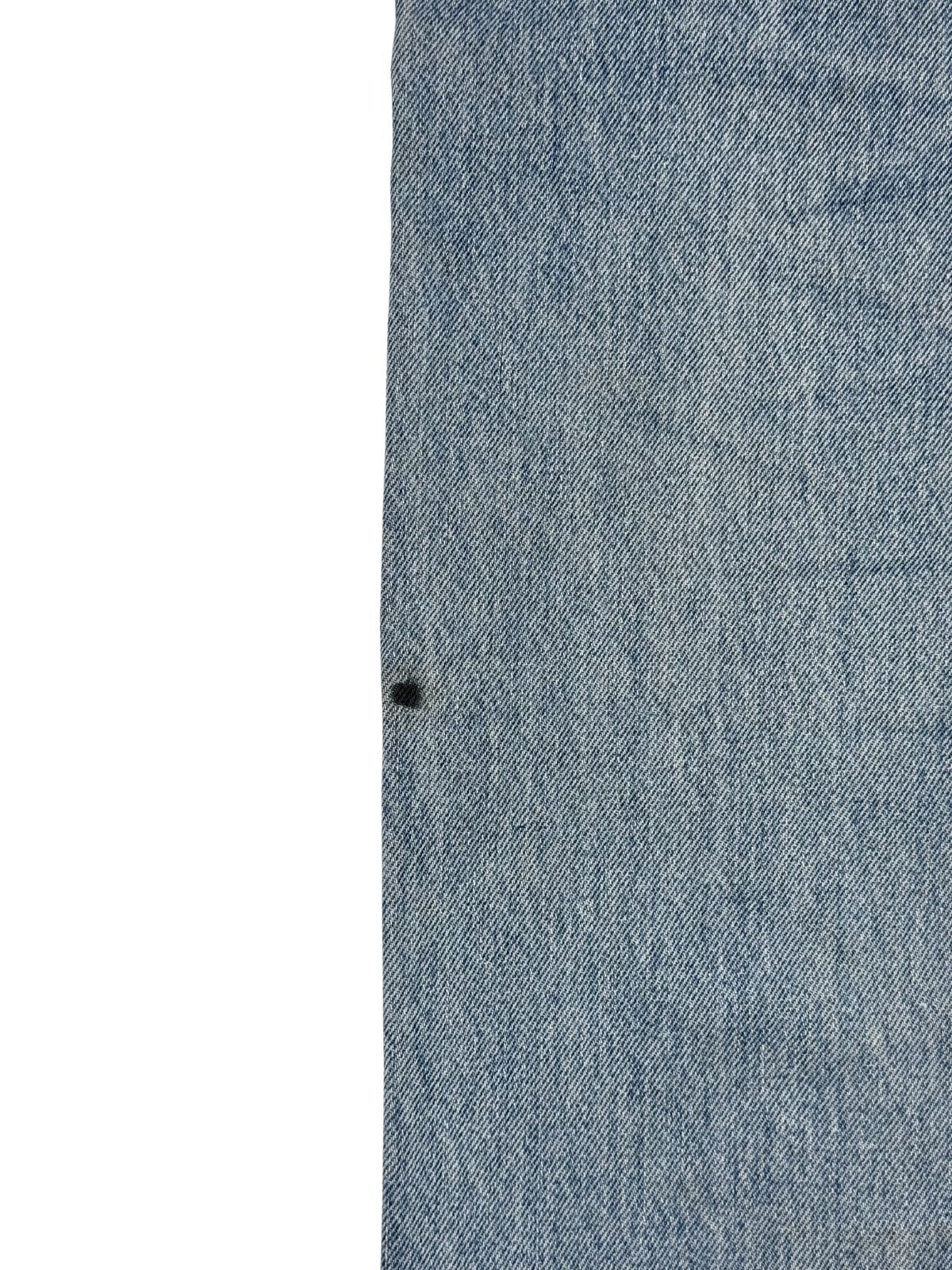 Makroaufnahme eines kleinen, tiefschwarzen Farbflecks auf dem hellblauen Jeansstoff zur transparenten Dokumentation von Mängeln im Vintage-Shop.