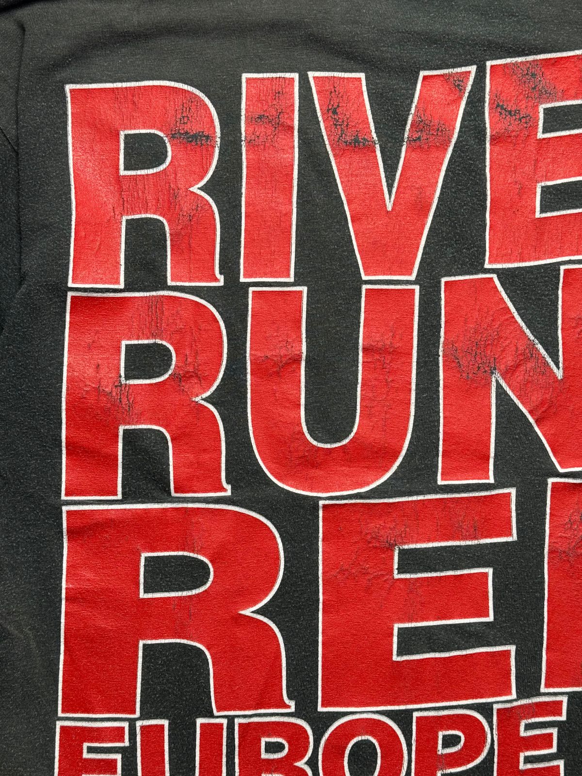 Detailansicht des leicht rissigen, authentisch gealterten Siebdrucks mit dem „RIVER RUNS RED“-Schriftzug auf dem Rücken.