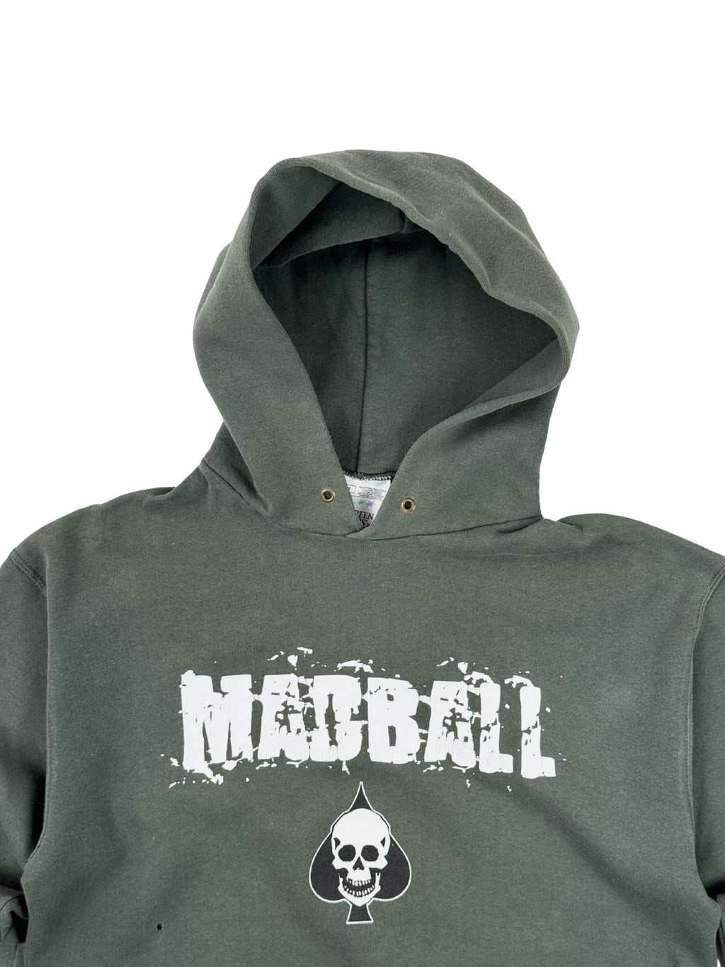 Detailansicht des Kragen- und Brustbereichs des Madball-Hoodies. Zu sehen sind der rissige weiße Print, die Kapuze mit metallenen Kordelösen (Ösen ohne Kordel) und das im Ausschnitt sichtbare weiße Nackenetikett.