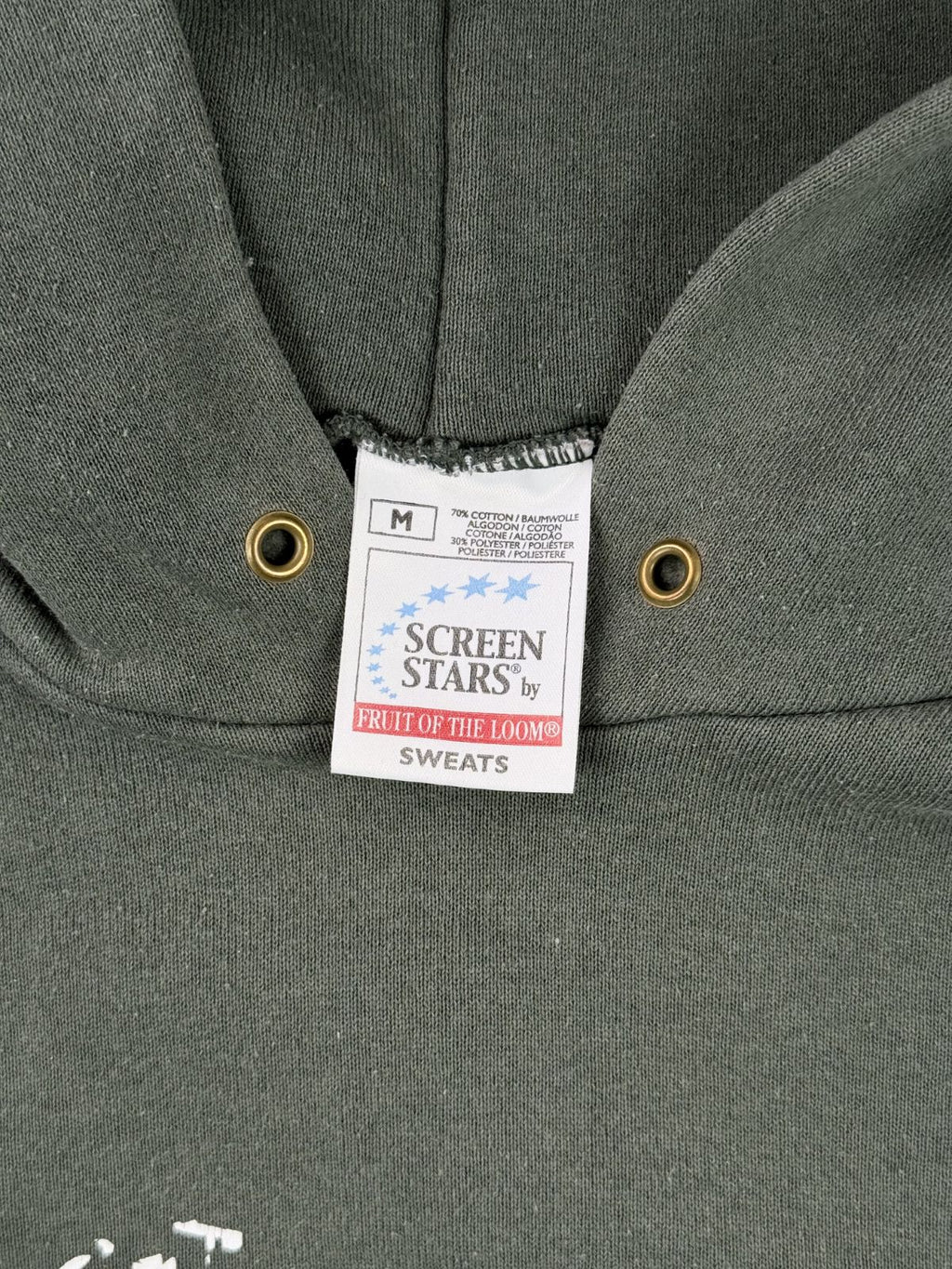 Makroaufnahme des Nackenlabels. Das weiße Stoffetikett der Marke „Screen Stars by Fruit of the Loom (Sweats)“ zeigt die Größe M, die Materialzusammensetzung (70% Baumwolle, 30% Polyester) und den Herkunftshinweis.