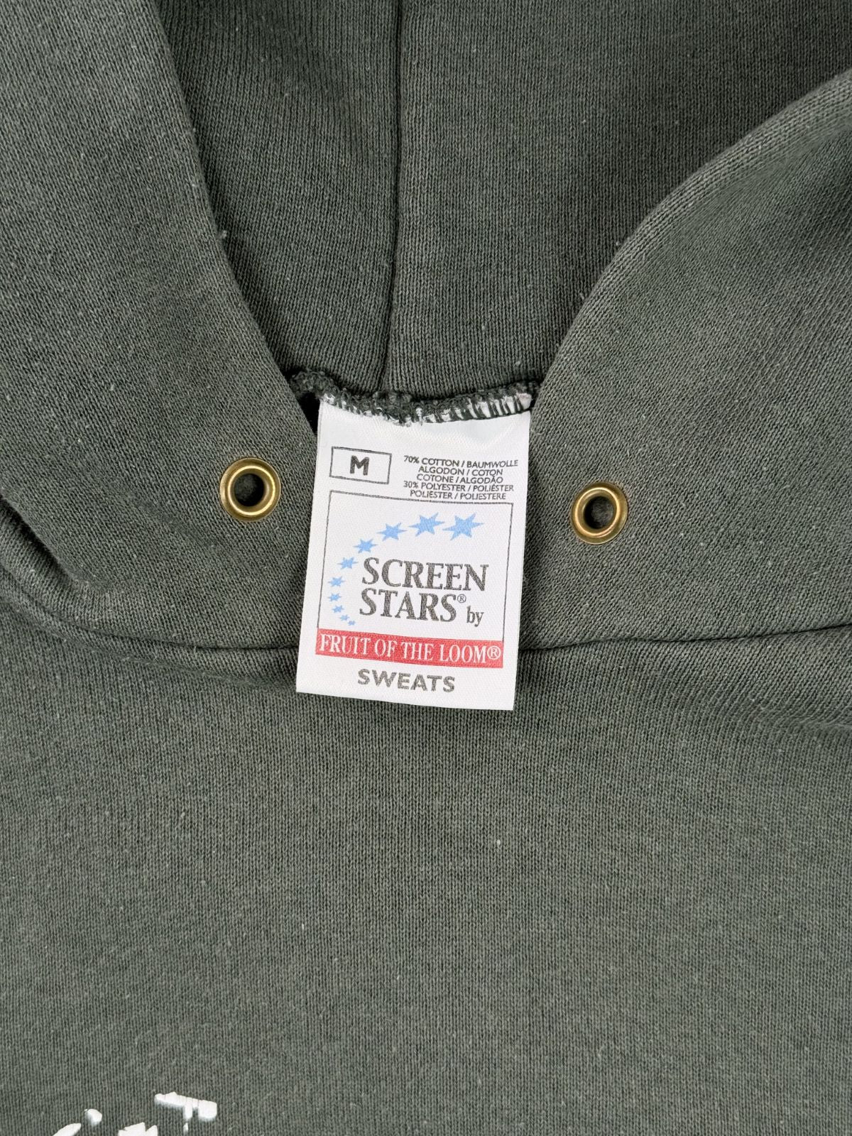 Makroaufnahme des Nackenlabels. Das weiße Stoffetikett der Marke „Screen Stars by Fruit of the Loom (Sweats)“ zeigt die Größe M, die Materialzusammensetzung (70% Baumwolle, 30% Polyester) und den Herkunftshinweis.
