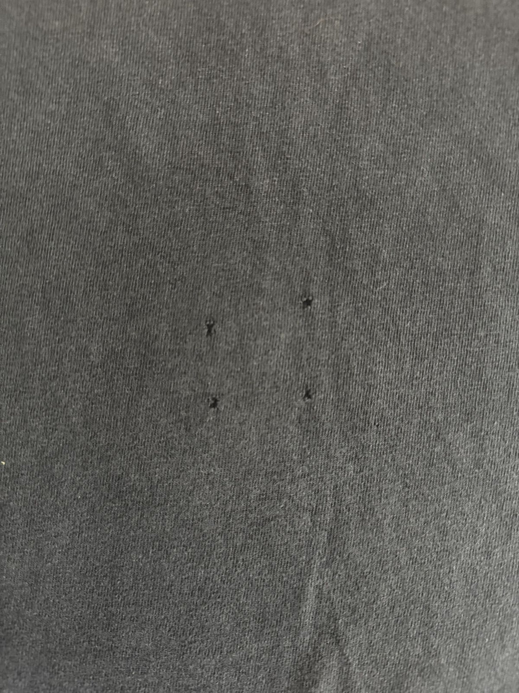 Makroaufnahme des Baumwollstoffs mit vier winzigen, quadratisch angeordneten Pinholes (Löchern) zur transparenten Zustandsdokumentation im Shop.