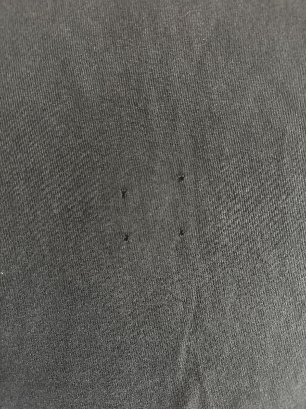Makroaufnahme des Baumwollstoffs mit vier winzigen, quadratisch angeordneten Pinholes (Löchern) zur transparenten Zustandsdokumentation im Shop.