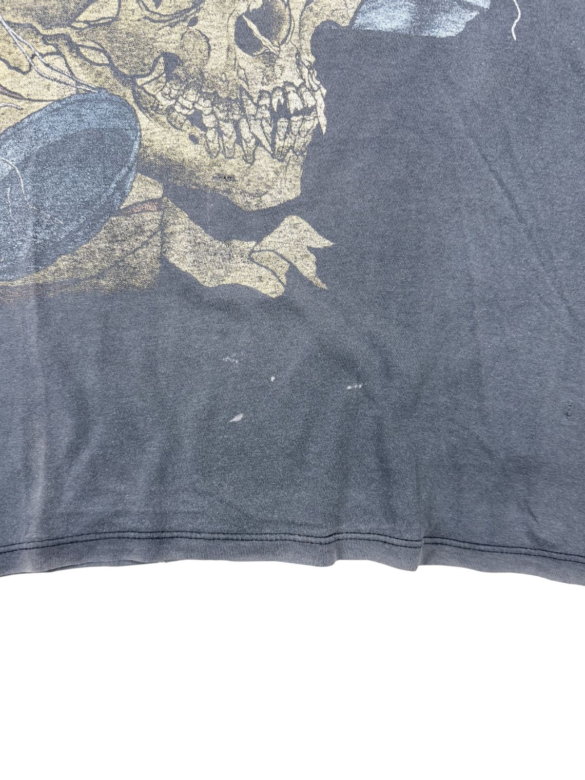 Makroaufnahme des Stoffes; zeigt kleine weiße Farbspritzer oder Flecken auf dem sonnengebleichten Material, die den individuellen Charakter des Shirts unterstreichen.