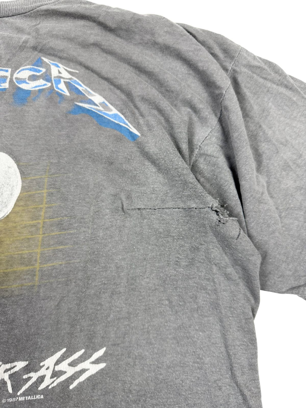 Detailansicht einer alten, handgenähten Reparaturstelle (Stitch-Repair) auf der Rückseite des grauen Metallica Shirts.