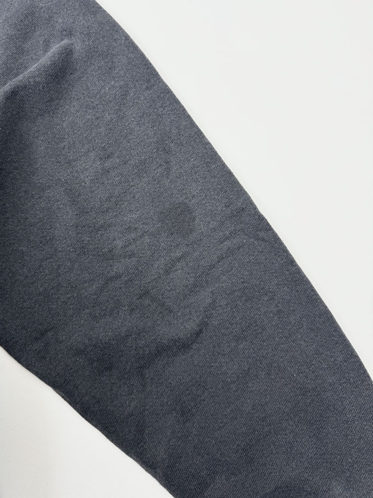 Detailaufnahme des schwarzen Vintage-Hoodie-Stoffs eines Ärmels (vermutlich der rechte, ohne Aufdruck) mit Fokus auf die leicht verwaschene Baumwolltextur und eine kleine, dunkle Verfärbung auf weißem Hintergrund.
