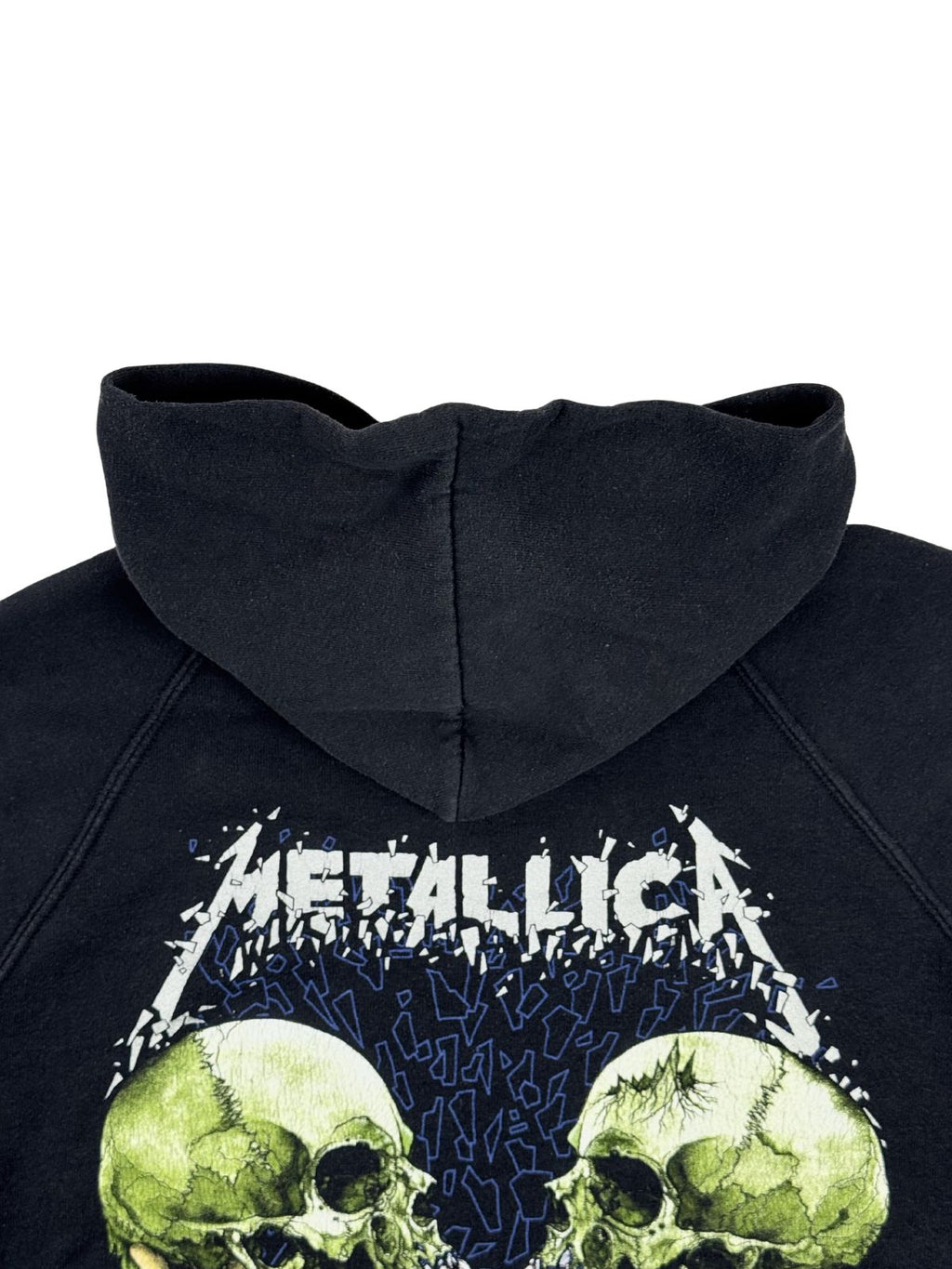 Detailansicht der oberen Rückseite des Hoodies mit Fokus auf den Übergang von der Kapuze zum großen, weißen Metallica-Schriftzug und den grünen Totenköpfen des Backprints.