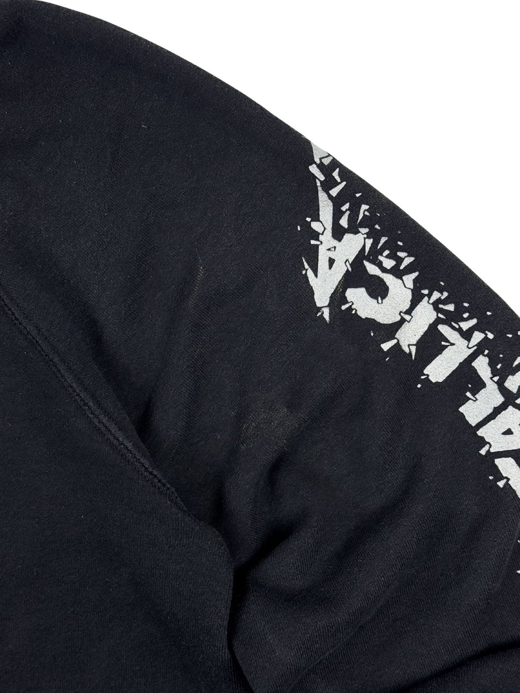Nahansicht des linken Ärmels zur Zustandsprüfung. Neben dem weißen Grafik-Print zeigt der schwarze Sweatstoff leichte, hellere Abriebspuren oder Flecken im Oberarmbereich.