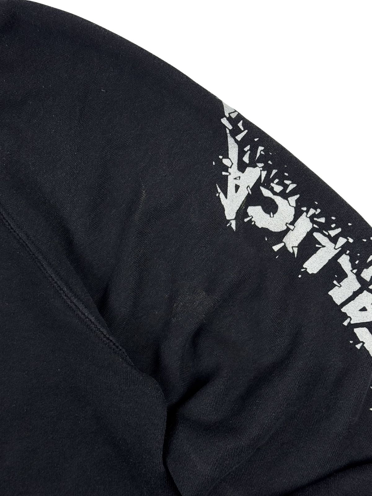 Nahansicht des linken Ärmels zur Zustandsprüfung. Neben dem weißen Grafik-Print zeigt der schwarze Sweatstoff leichte, hellere Abriebspuren oder Flecken im Oberarmbereich.