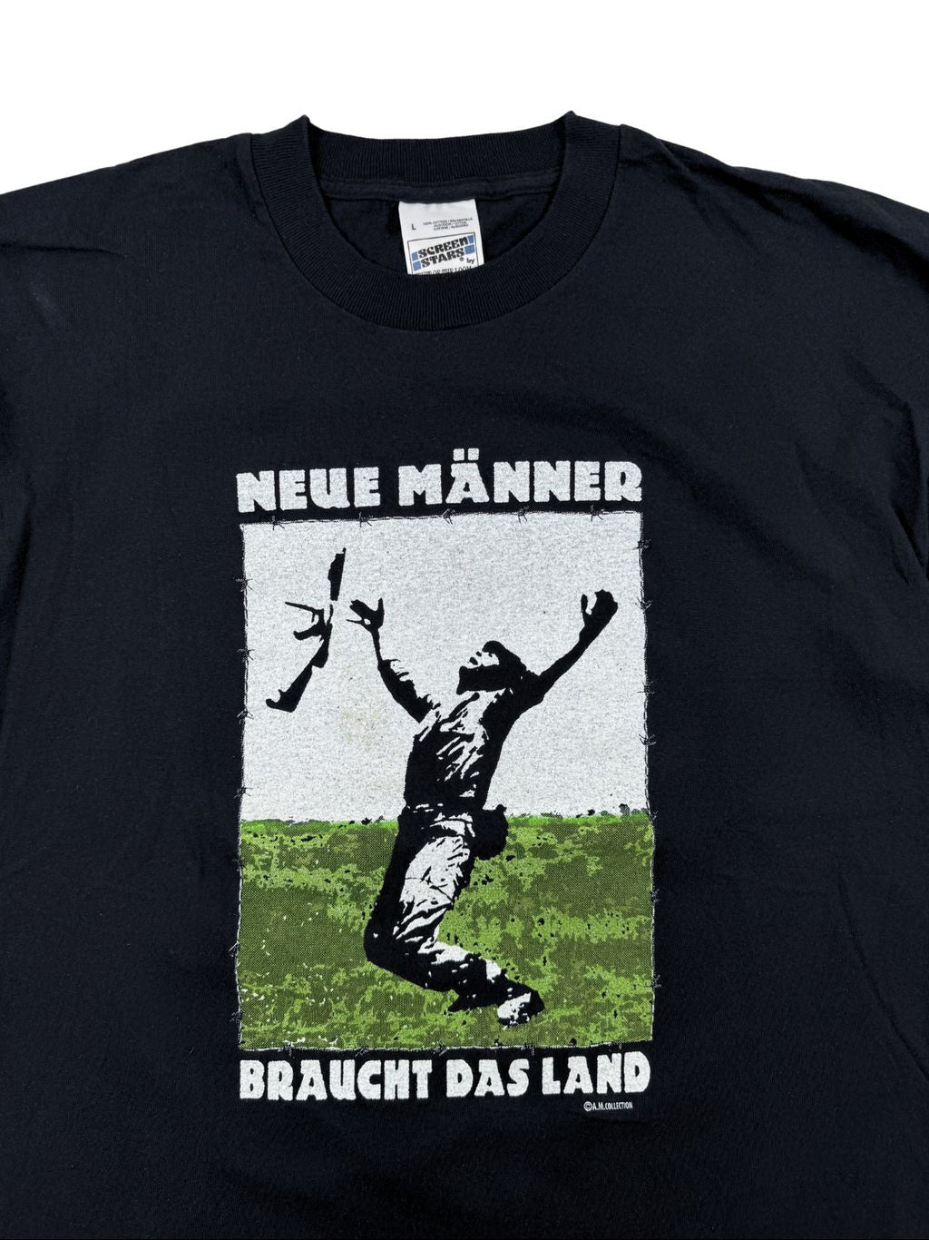 Nahaufnahme der Vorderseite des Shirts mit dem kontrastreichen, leicht rissigen Siebdruck-Motiv und dem Slogan „NEUE MÄNNER BRAUCHT DAS LAND“ über dem Rundhalskragen.