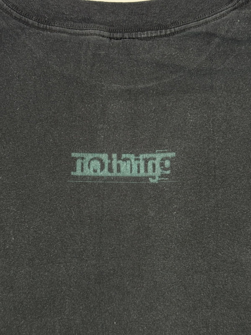 Detailaufnahme des minimalistischen, grünen „nothing“-Schriftzugs auf dem schwarzen Baumwollstoff der Rückseite.