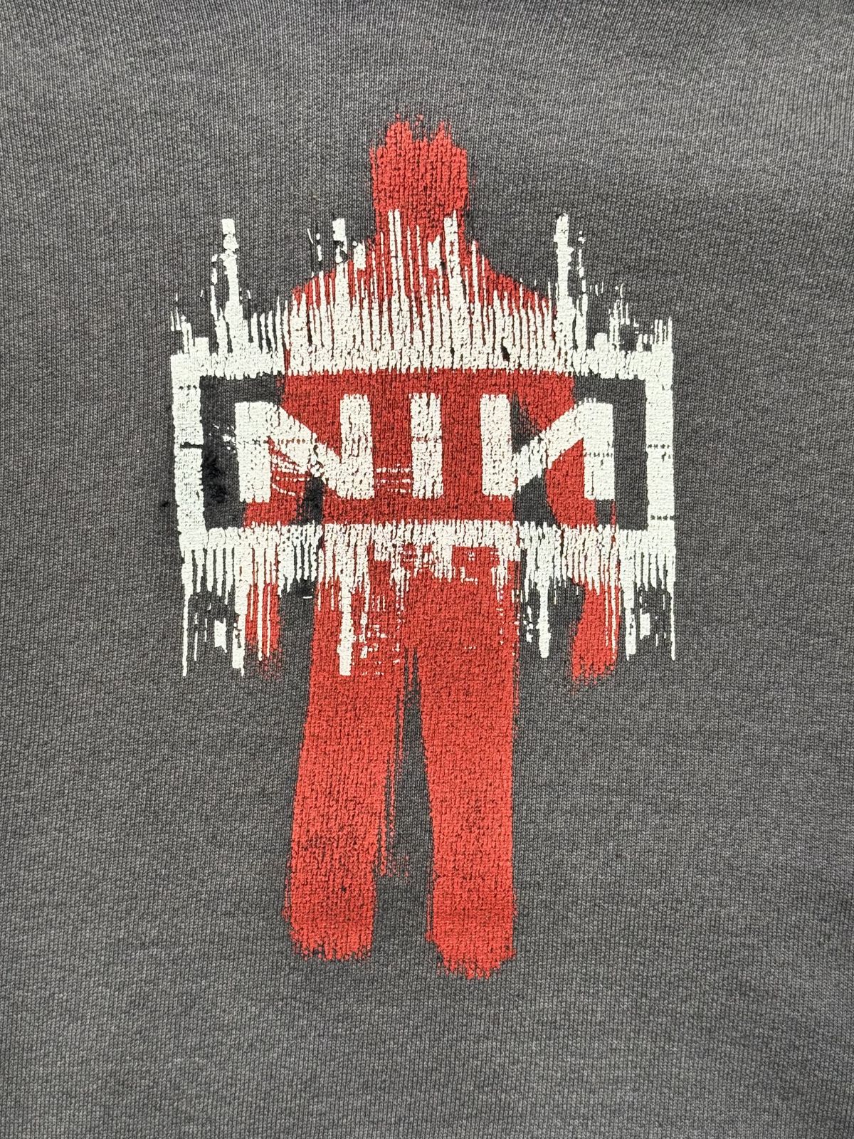 Detailansicht des vorderen Grafikprints mit der roten Personen-Silhouette und dem charakteristischen, weiß-schwarzen NIN-Kasten-Logo im Used-Look.