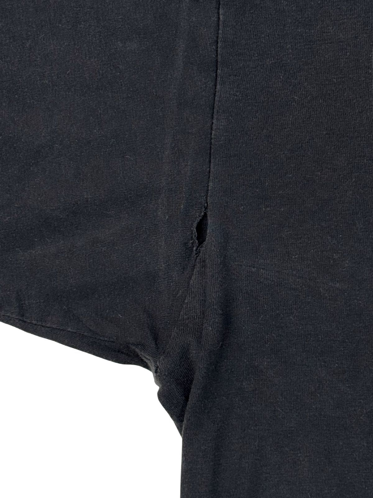 Nahaufnahme eines Lochs an der Achselnaht (Armpit Hole) des verwaschenen schwarzen Primus T-Shirts von 1995. Ein wichtiges Detail für Sammler zur genauen Einschätzung des Vintage-Zustands.