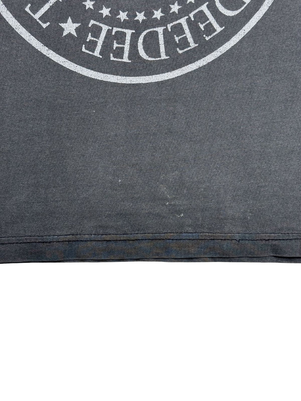 Detailansicht des unteren vorderen Saums des ausgewaschenen, grauen Ramones-Shirts mit doppelter Naht und leichten Verfärbungen bzw. Tragespuren am Stoff.