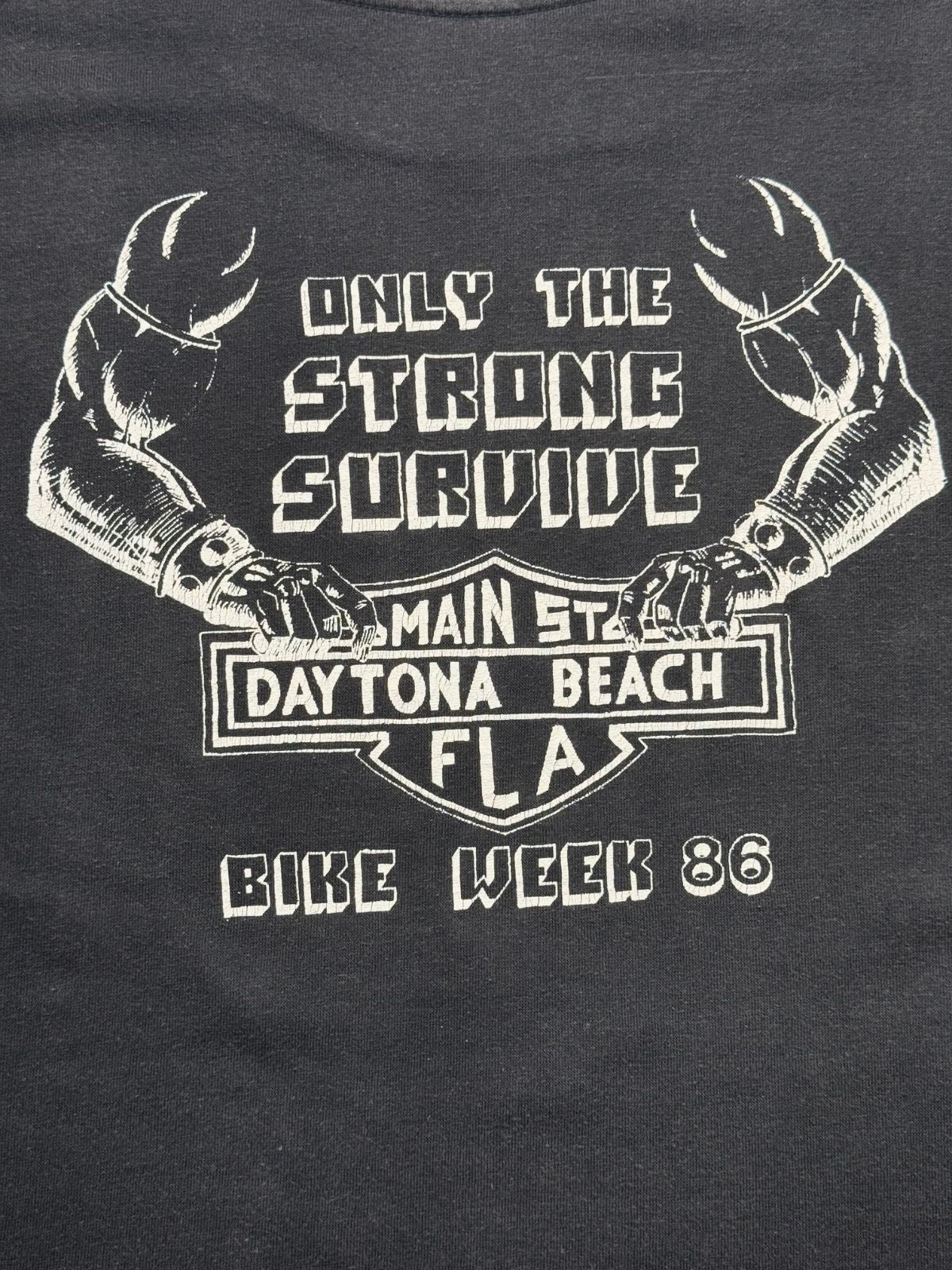 Detaillierte Ansicht des Rückenprints mit muskulösen Biker-Armen, Nietenbändern, Harley-Schild-Emblem und dem Slogan „ONLY THE STRONG SURVIVE - BIKE WEEK 86“.