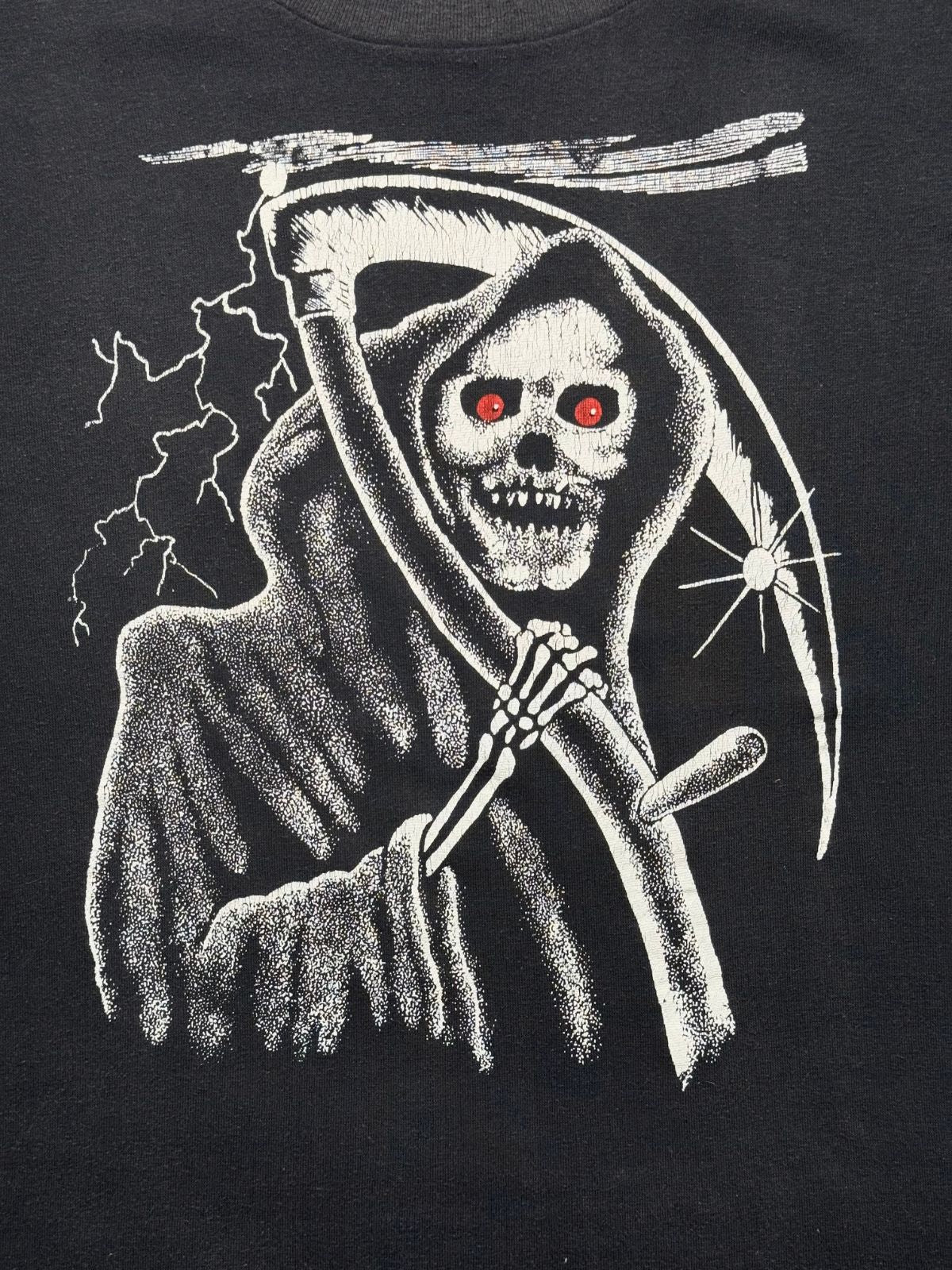 Detailansicht des vorderen Siebdrucks mit dem unheimlichen Sensemann (Grim Reaper), Blitzen und leuchtend roten Augen auf schwarzem Baumwollstoff.