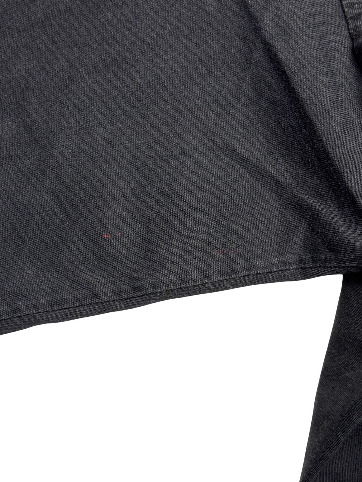 Detailaufnahme des Ärmelstoffes mit winzigen, unauffälligen roten Farbspritzern bzw. Flecken im Baumwollmaterial.