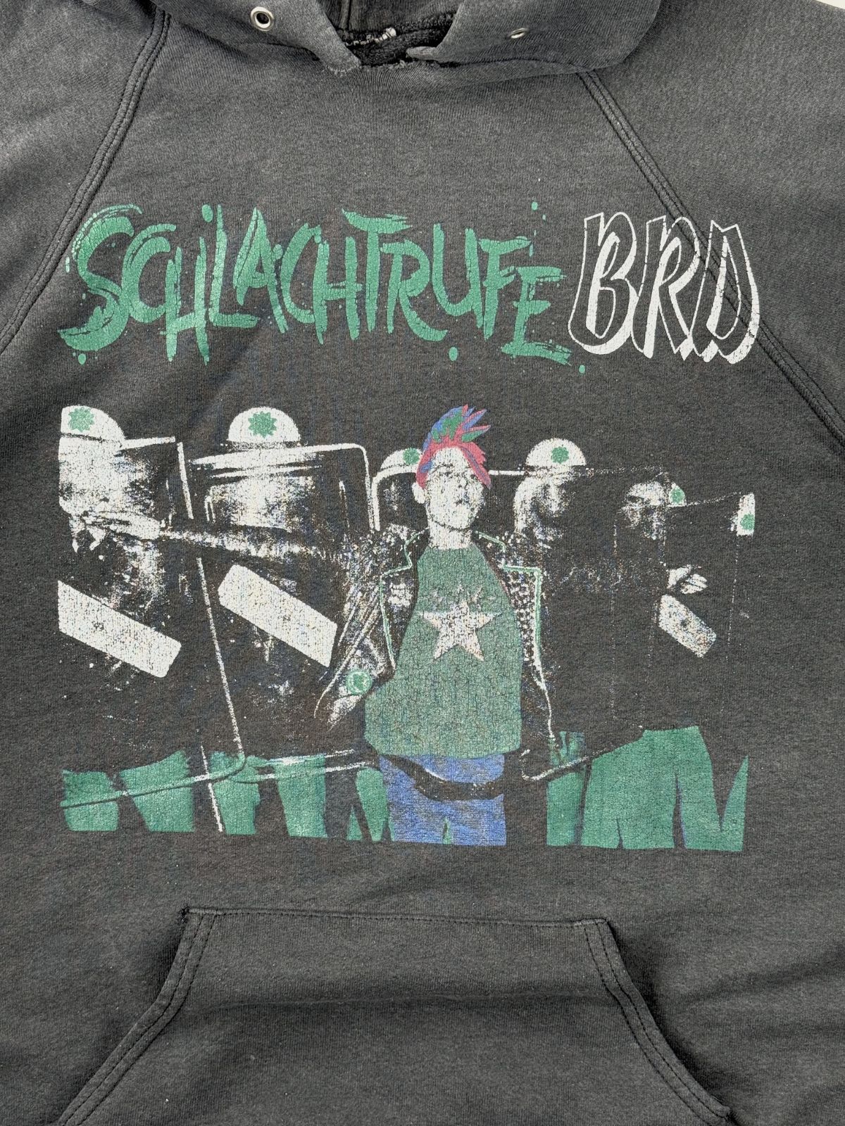 Detailansicht des vorderen Siebdrucks. Zu sehen ist der zweifarbige Schriftzug „SCHLACHTRUFE BRD“ über einer Grafik, die einen Punk mit buntem Irokesenschnitt vor einer Reihe von Polizisten mit Einsatzschilden zeigt.
