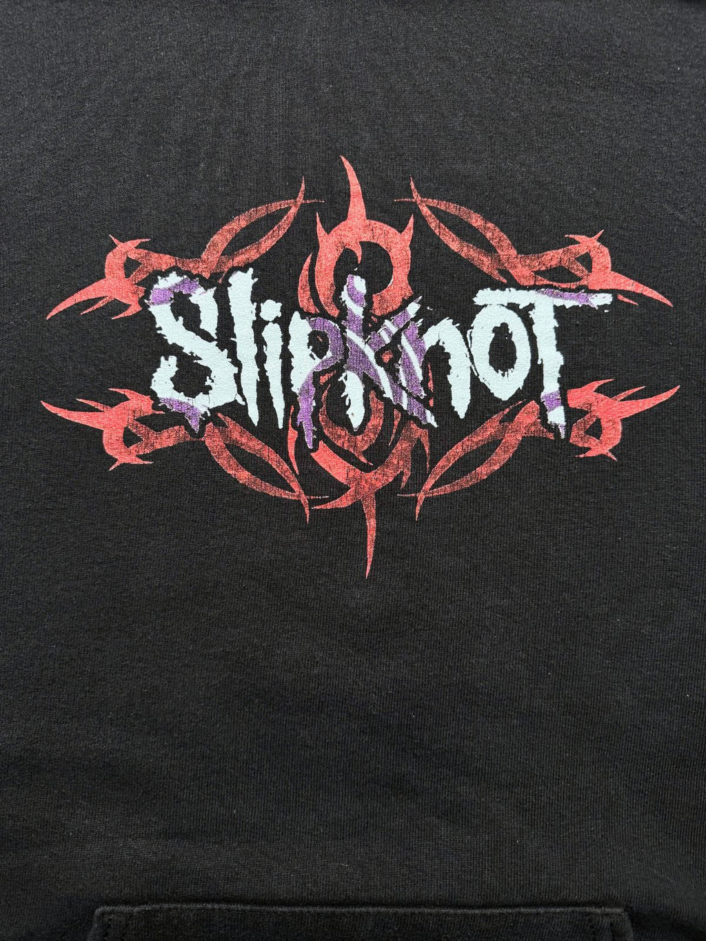 Nahaufnahme des Brustprints mit weiß-lila „Slipknot“-Schriftzug vor rotem Tribal-Rahmen und dem charakteristischen Band-Symbol.