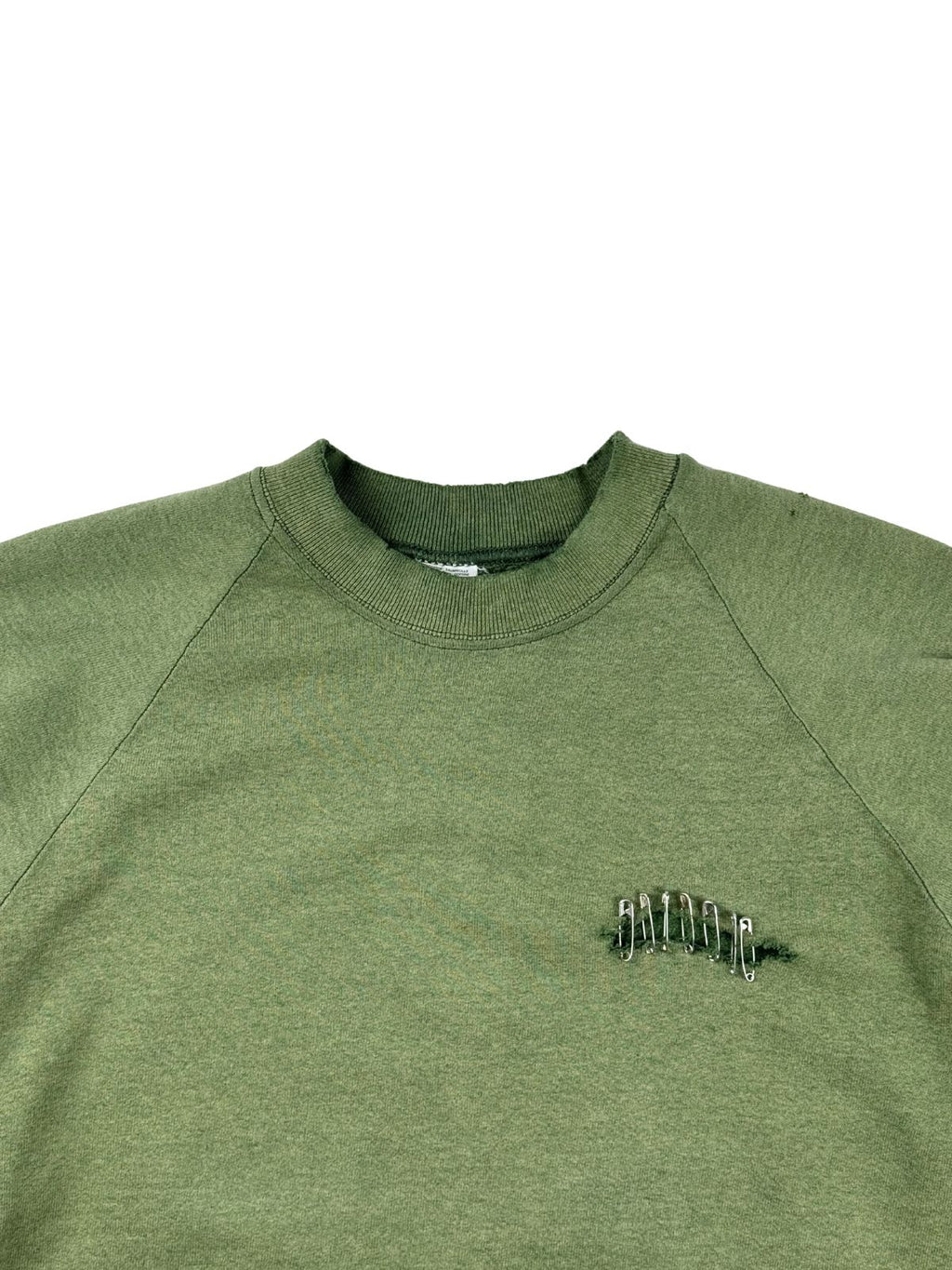 Detailansicht der Vorderseite des olivgrünen Pullovers mit Fokus auf den gerippten Rundhalsausschnitt und den mit Sicherheitsnadeln fixierten Riss.