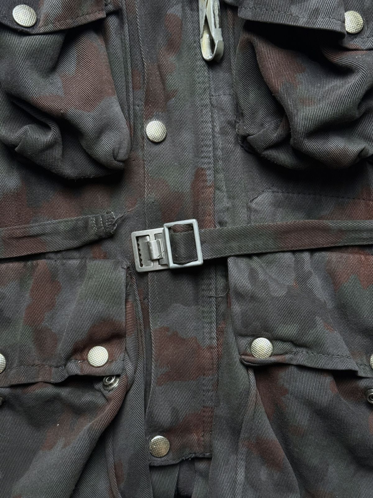 Detailaufnahme der militärischen Metall-Hardware und Haken, die zur Fixierung des Rucksacks an der Jacke dienen.