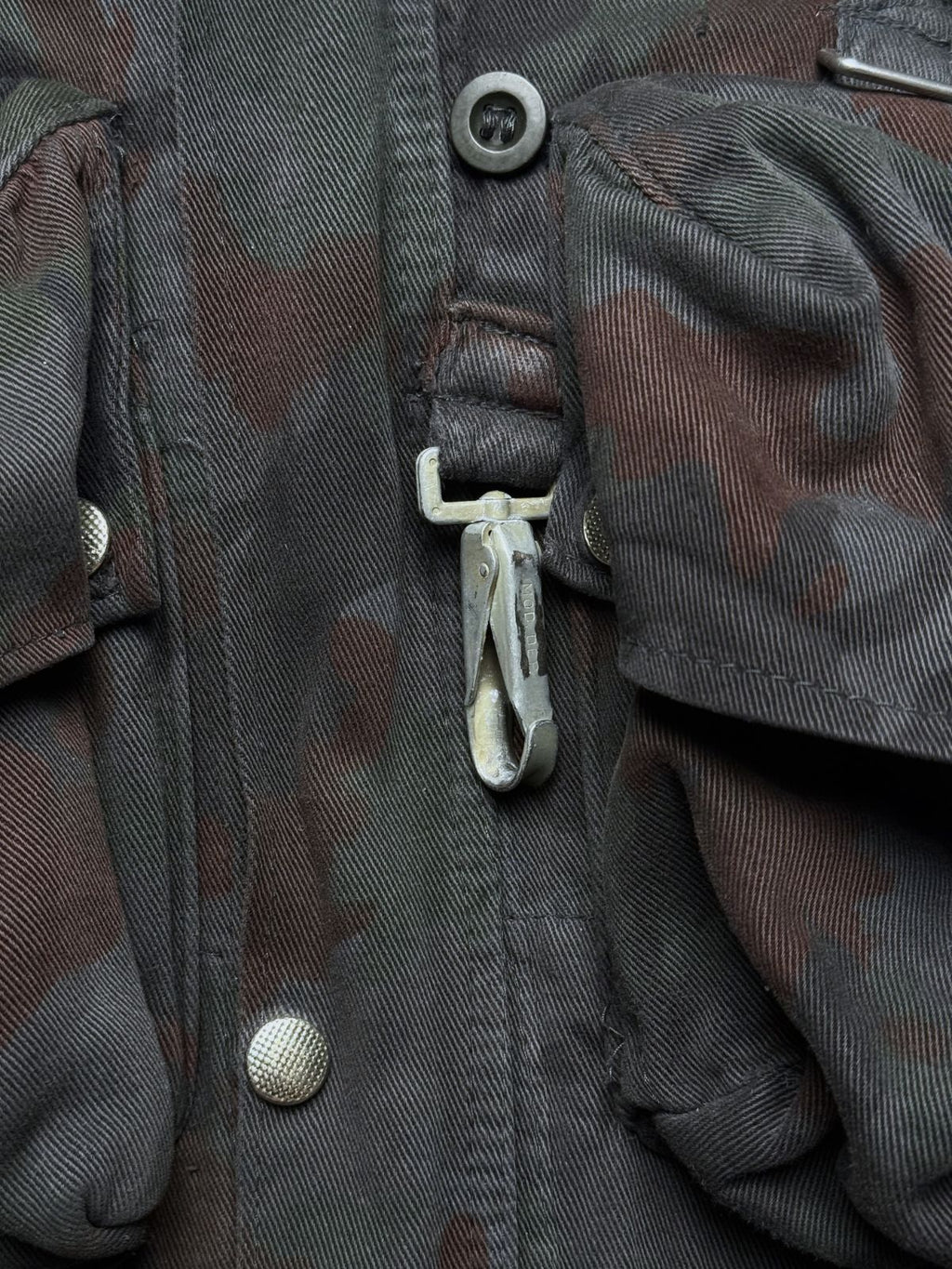 Detailansicht des massiven Metall-Karabiners auf der Frontseite der Schweizer M70-Feldjacke zur Befestigung von Ausrüstungsteilen.