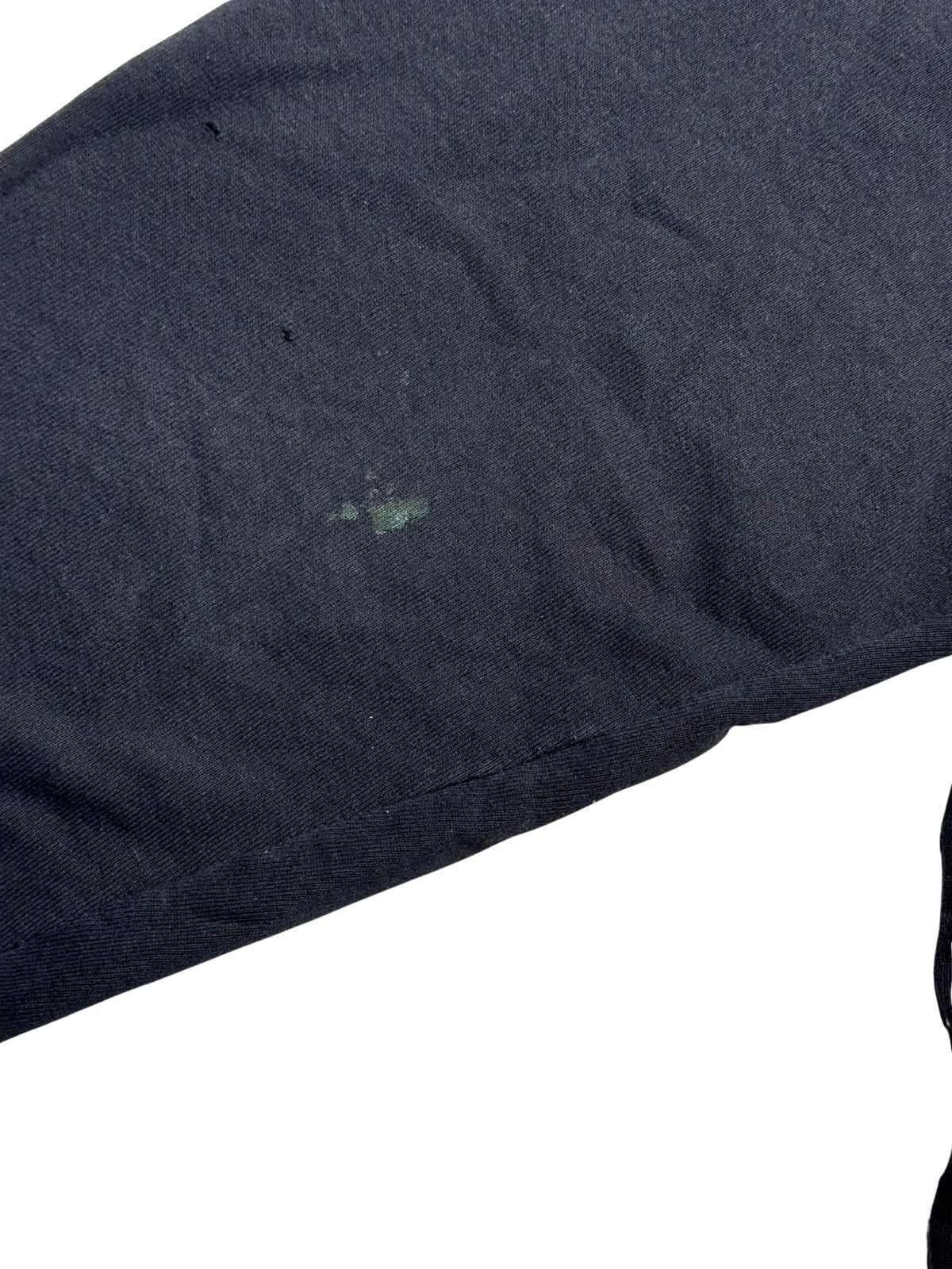 Nahaufnahme des Ärmels zur transparenten Zustandsdokumentation mit zwei feinen Pinholes und einem grünlich-hellen Fleck auf schwarzem Stoff.