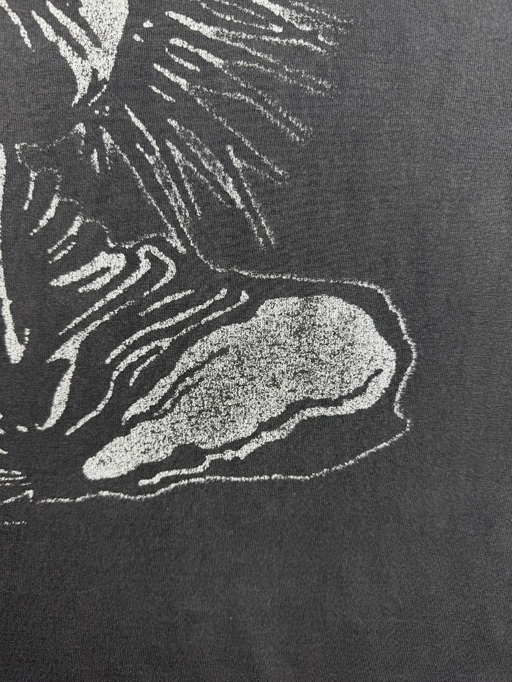 Detailansicht des vorderen Siebdrucks auf dem verwaschenen Baumwollstoff, die den unteren Teil der zerschlissenen Totenkopf-Grafik im distressed Look zeigt.