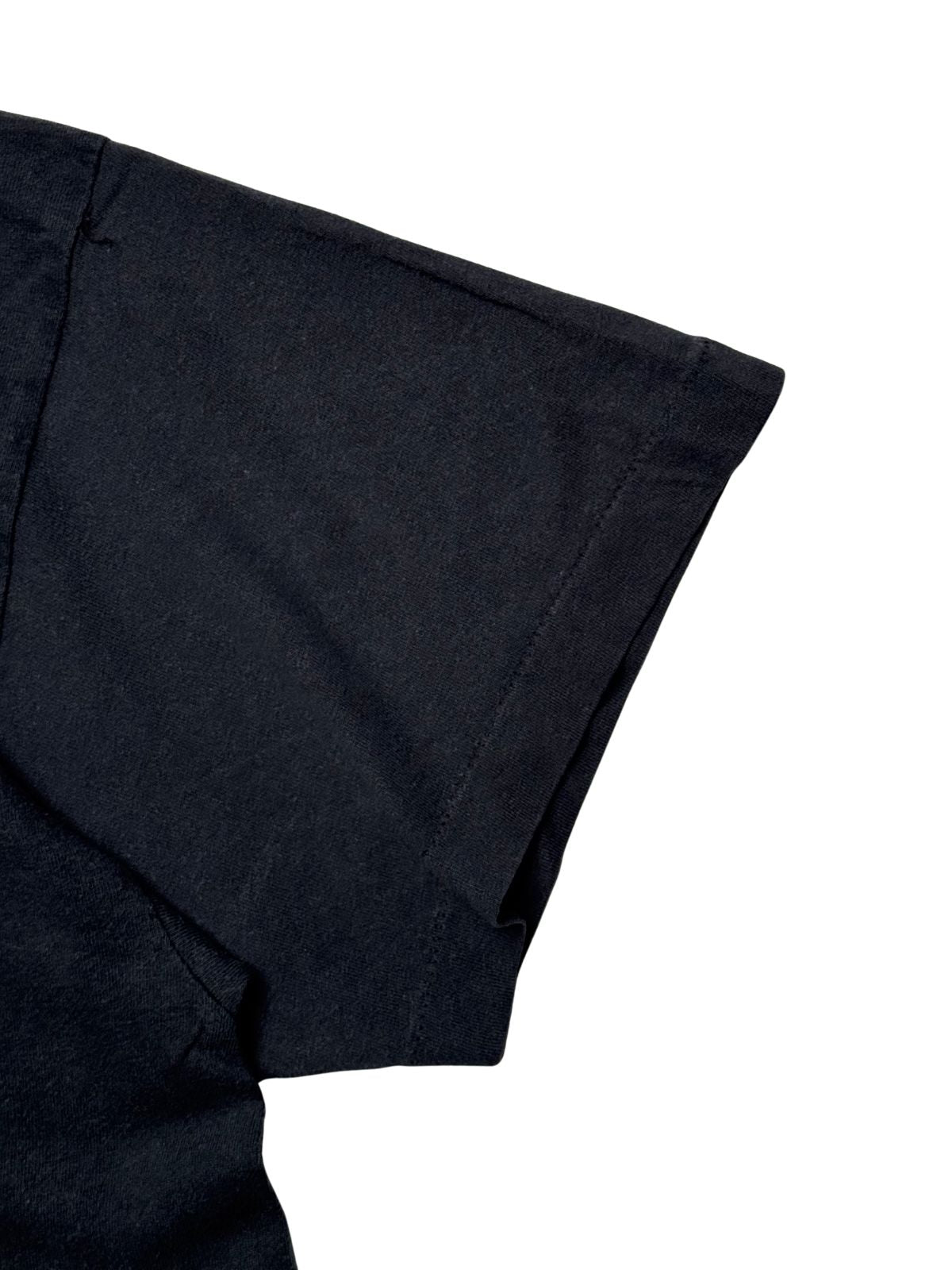 Detailansicht des kurzen Ärmels mit klassischer Single-Stitch-Einfachnaht am Ärmelbund auf dem schwarzen, leicht verwaschenen Baumwollstoff.