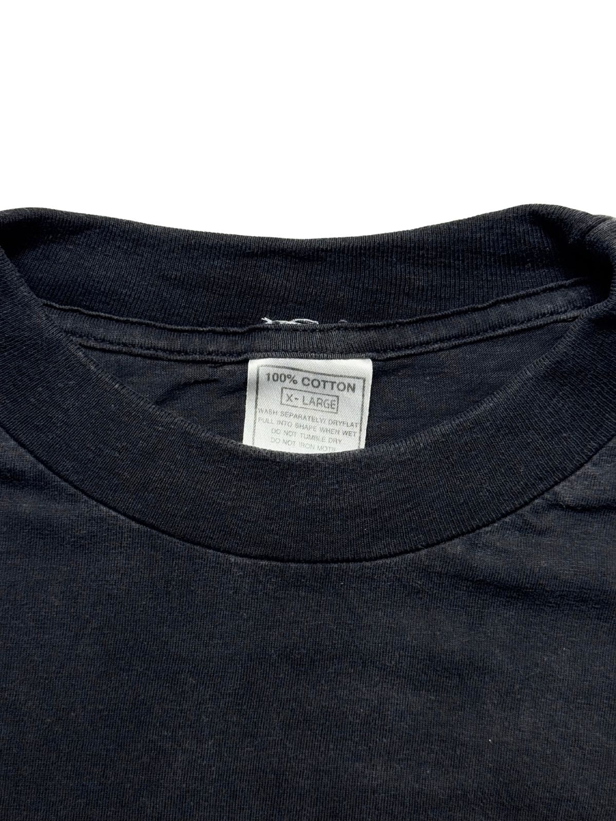 Nahaufnahme des Kragens mit dem originalen weißen Pflege-Etikett (100% COTTON / X-LARGE) auf dem schwarzen Baumwollstoff.