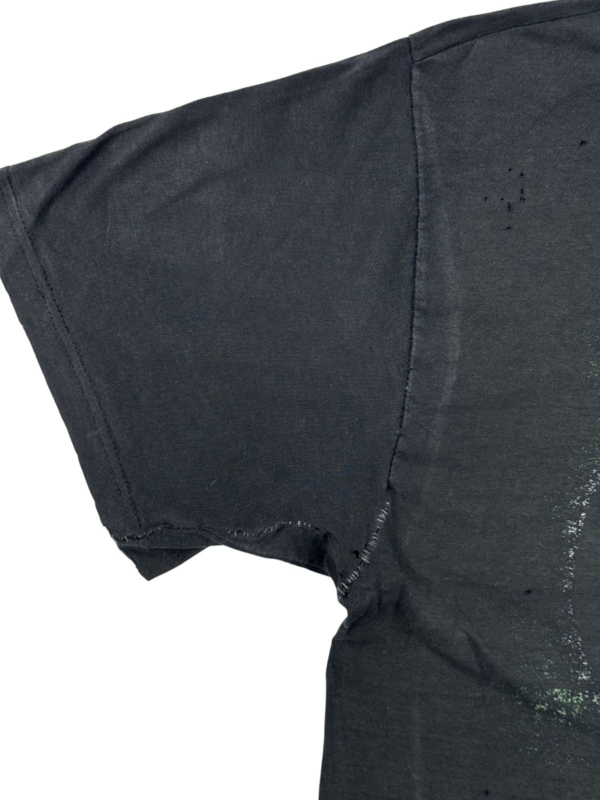 Nahaufnahme einer reparierten Naht unter der linken Achselhöhle auf der Rückseite des Vintage-Shirts. Zu sehen ist eine deutlich sichtbare, nachträglich mit schwarzem Garn per Hand geflickte Stelle entlang der Ärmelverbindung.
