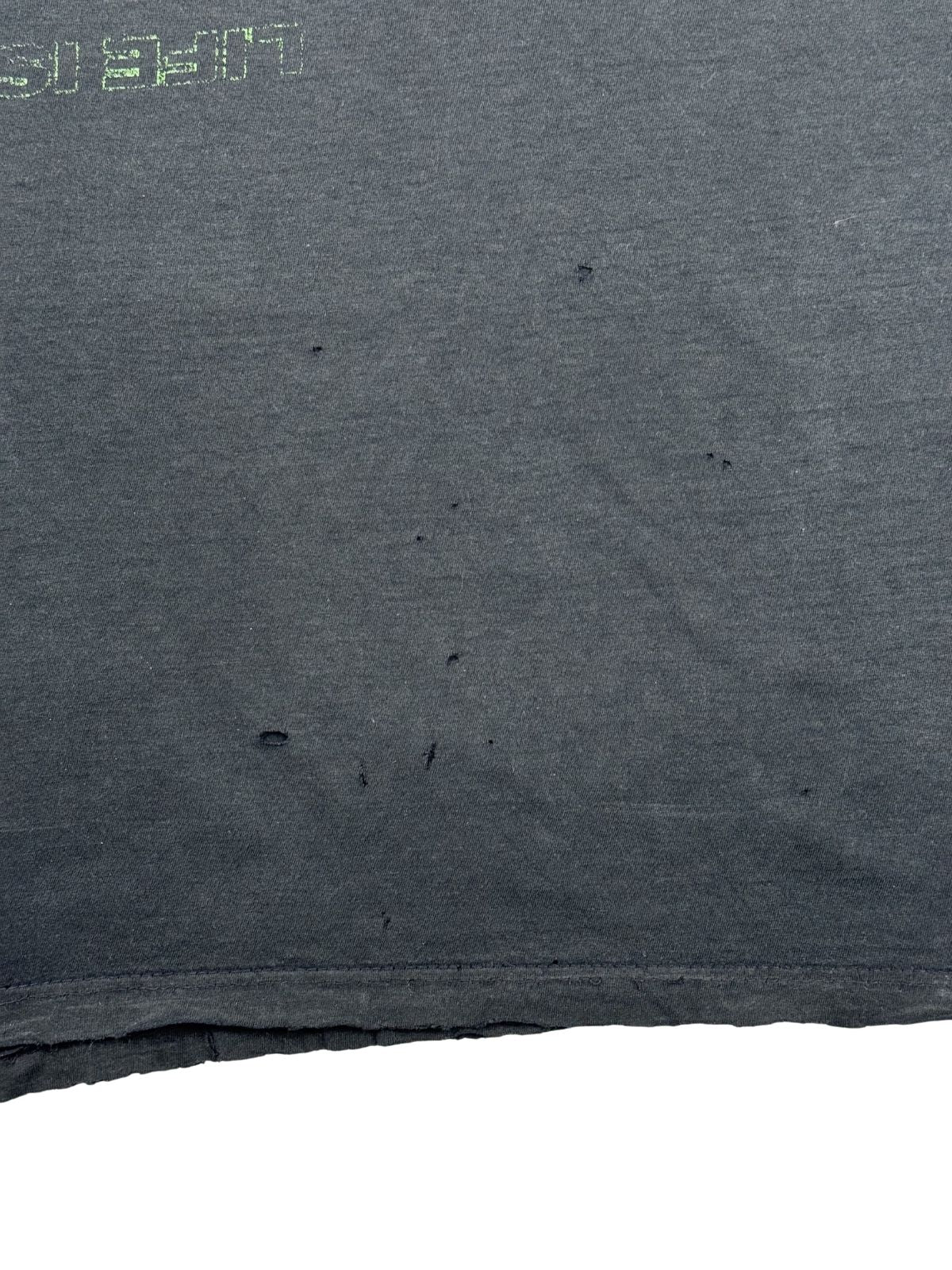 Nahaufnahme des unteren vorderen Bereichs des schwarzen Thrashed-Shirts. Zu sehen ist eine Ansammlung kleiner Löcher (Pinholes) knapp über dem ausgefransten, welligen Saum.