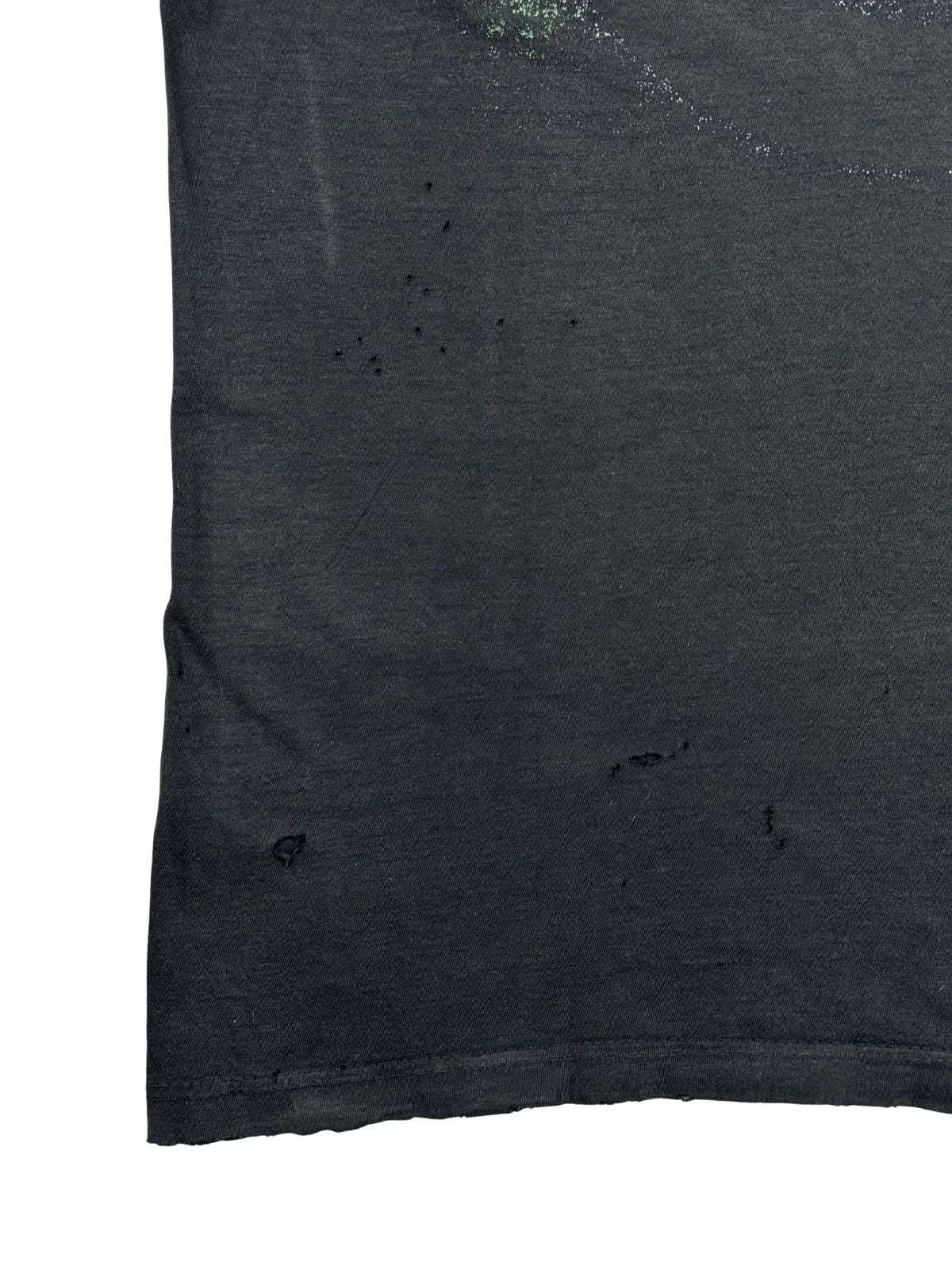 Nahansicht des unteren linken Rückenbereichs des T-Shirts mit einer Ansammlung von mehreren kleinen Löchern, sogenannten „Pinhois“, und einem leicht ausgefransten Saum.