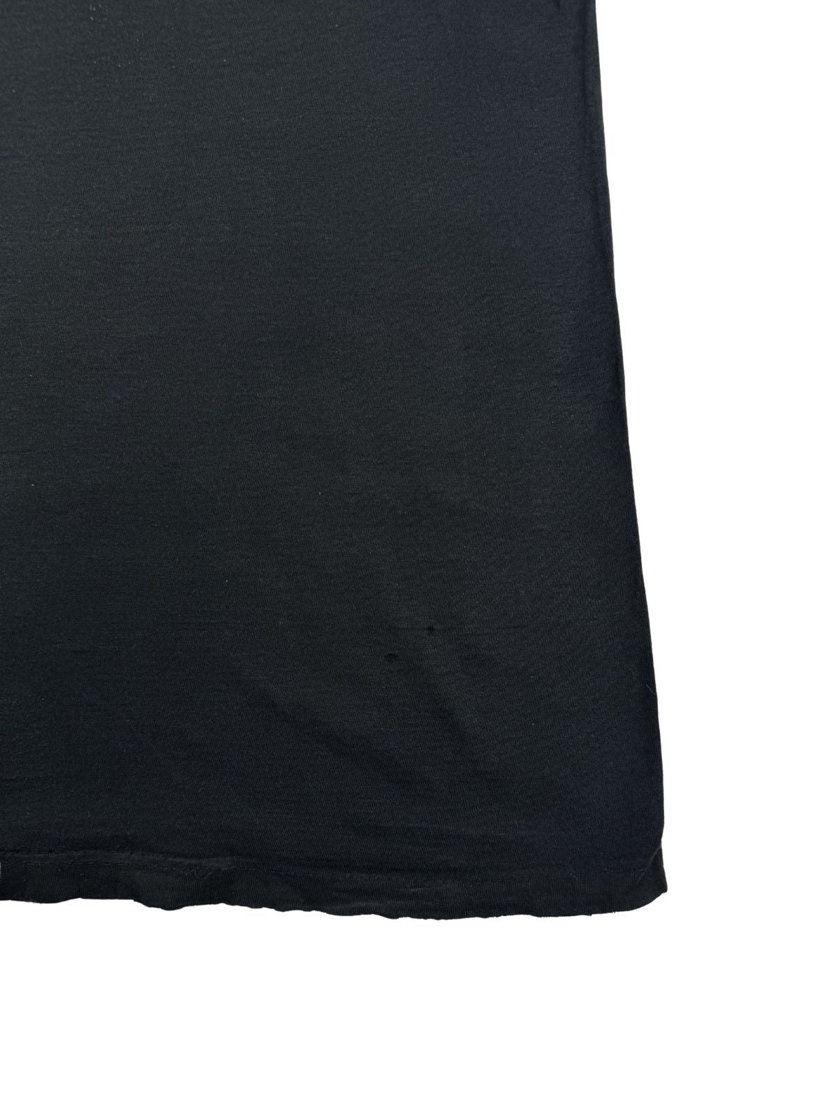 Detailansicht der unteren rechten Rückseite des T-Shirts zur Überprüfung des Zustands. Der schwarze Baumwollstoff weist in Saumnähe zwei minimale Löcher auf.