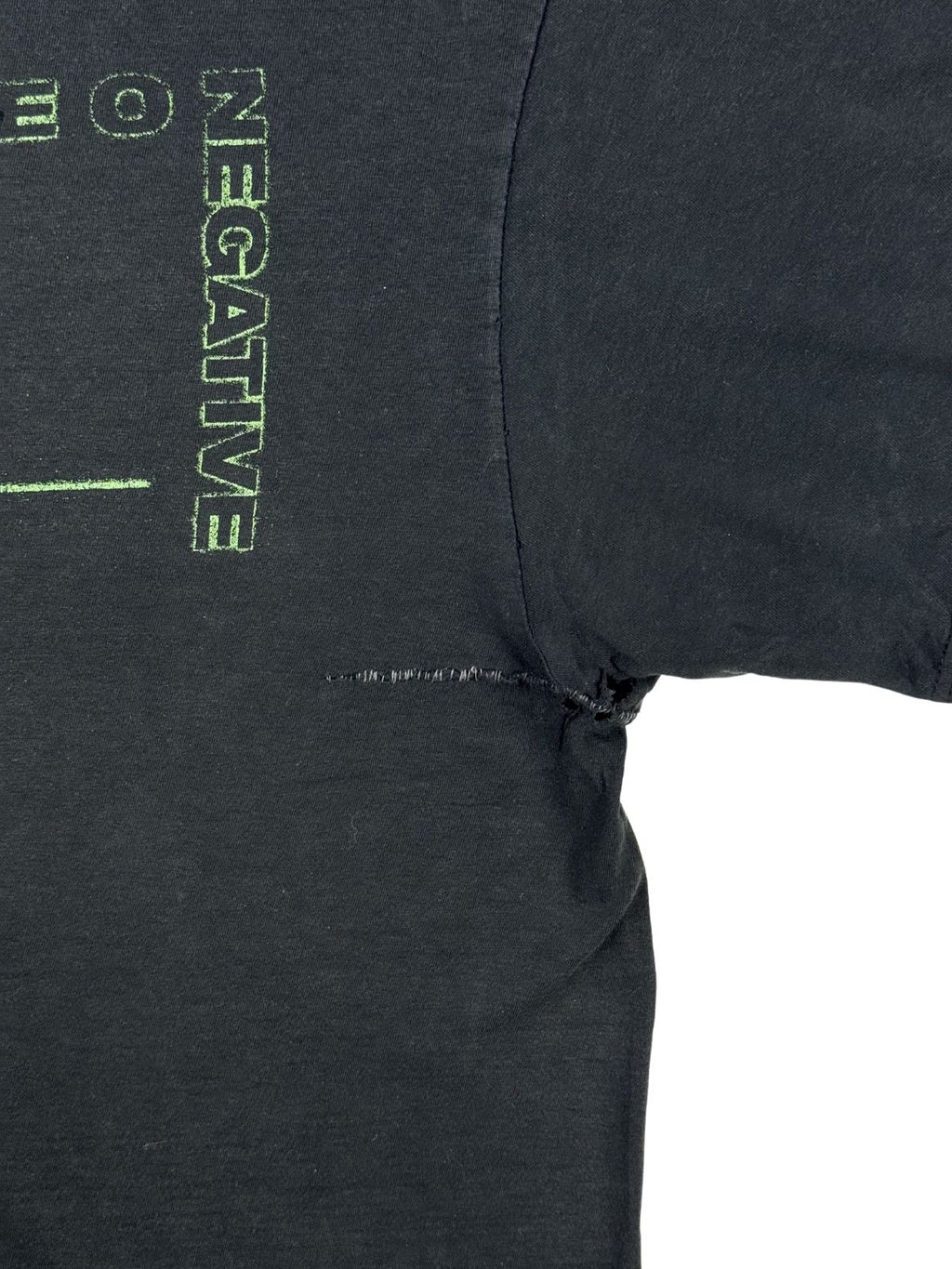 Nahaufnahme einer reparierten Stelle auf der Vorderseite neben dem „NEGATIVE“-Schriftzug. Zu sehen ist ein horizontaler Riss im schwarzen Stoff, der mit einer sichtbaren Naht geflickt wurde.