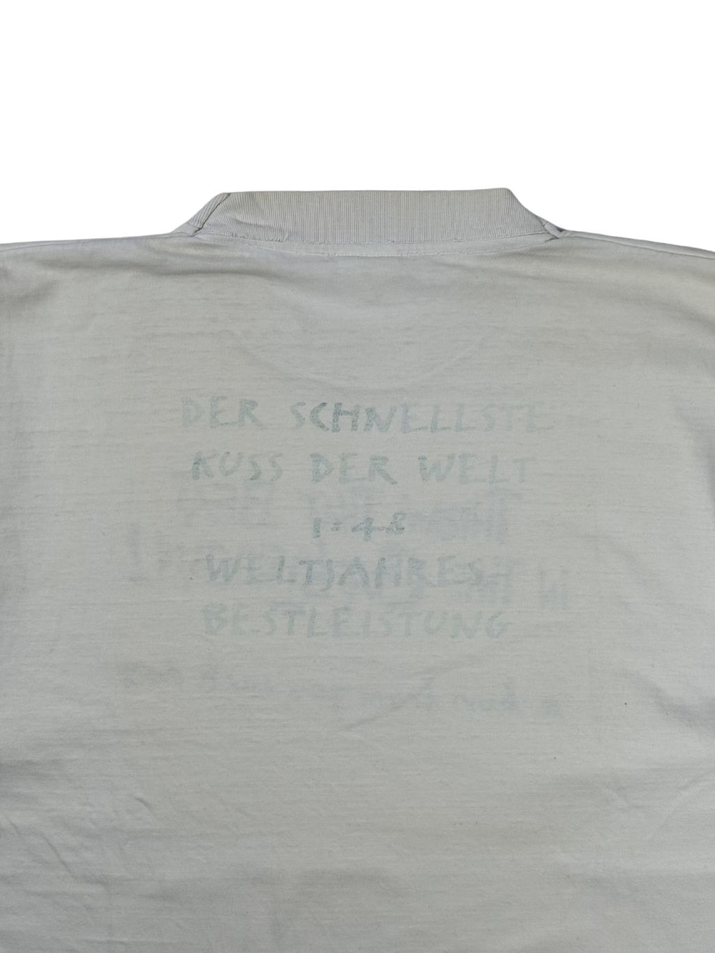 Nahaufnahme des Backprints auf der Rückseite des Throw That Beat T-Shirts. Der hellgraue Text lautet: „DER SCHNELLSTE KUSS DER WELT 1:48 WELTJAHRESBESTLEISTUNG“.