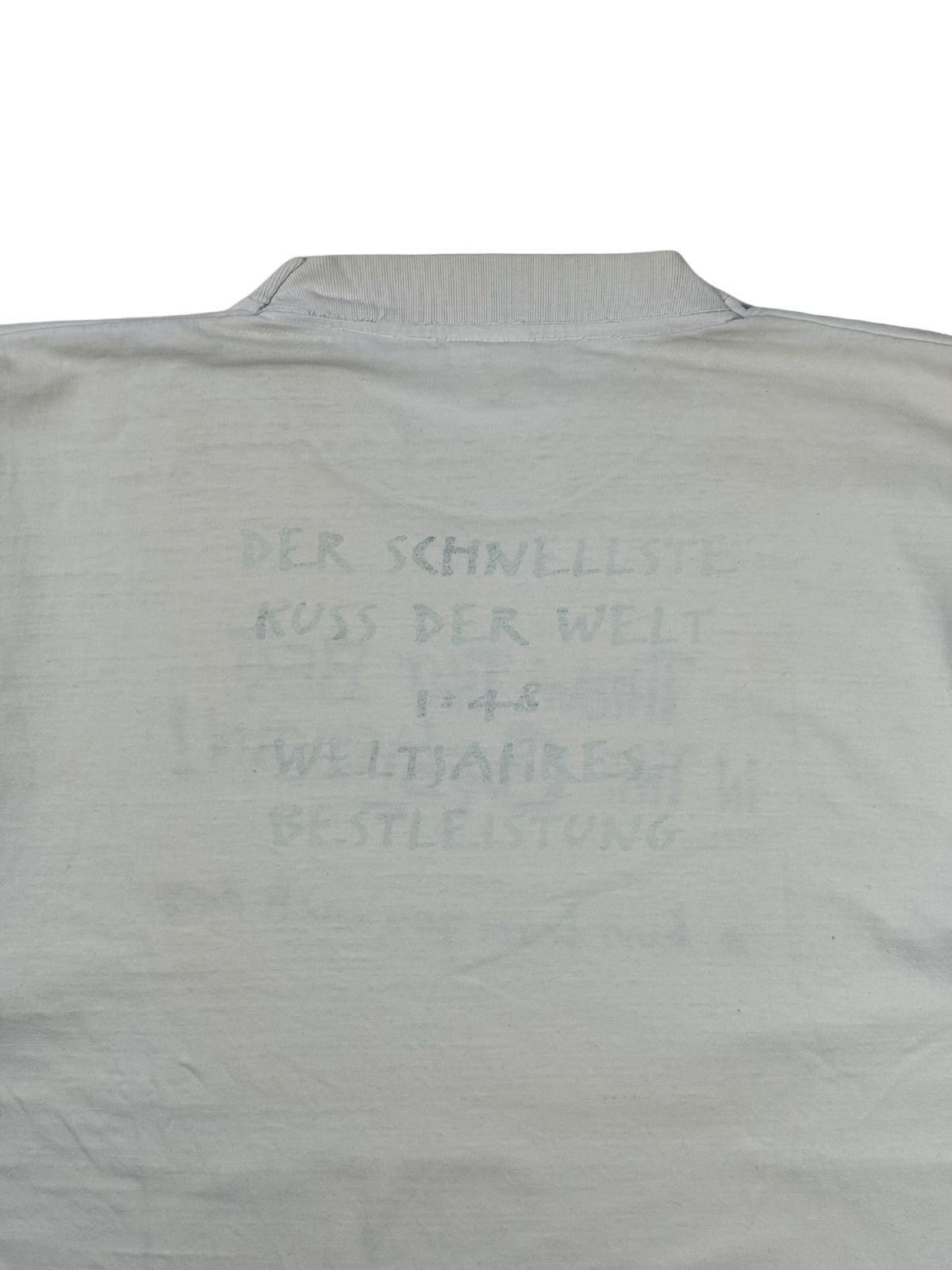 Nahaufnahme des Backprints auf der Rückseite des Throw That Beat T-Shirts. Der hellgraue Text lautet: „DER SCHNELLSTE KUSS DER WELT 1:48 WELTJAHRESBESTLEISTUNG“.