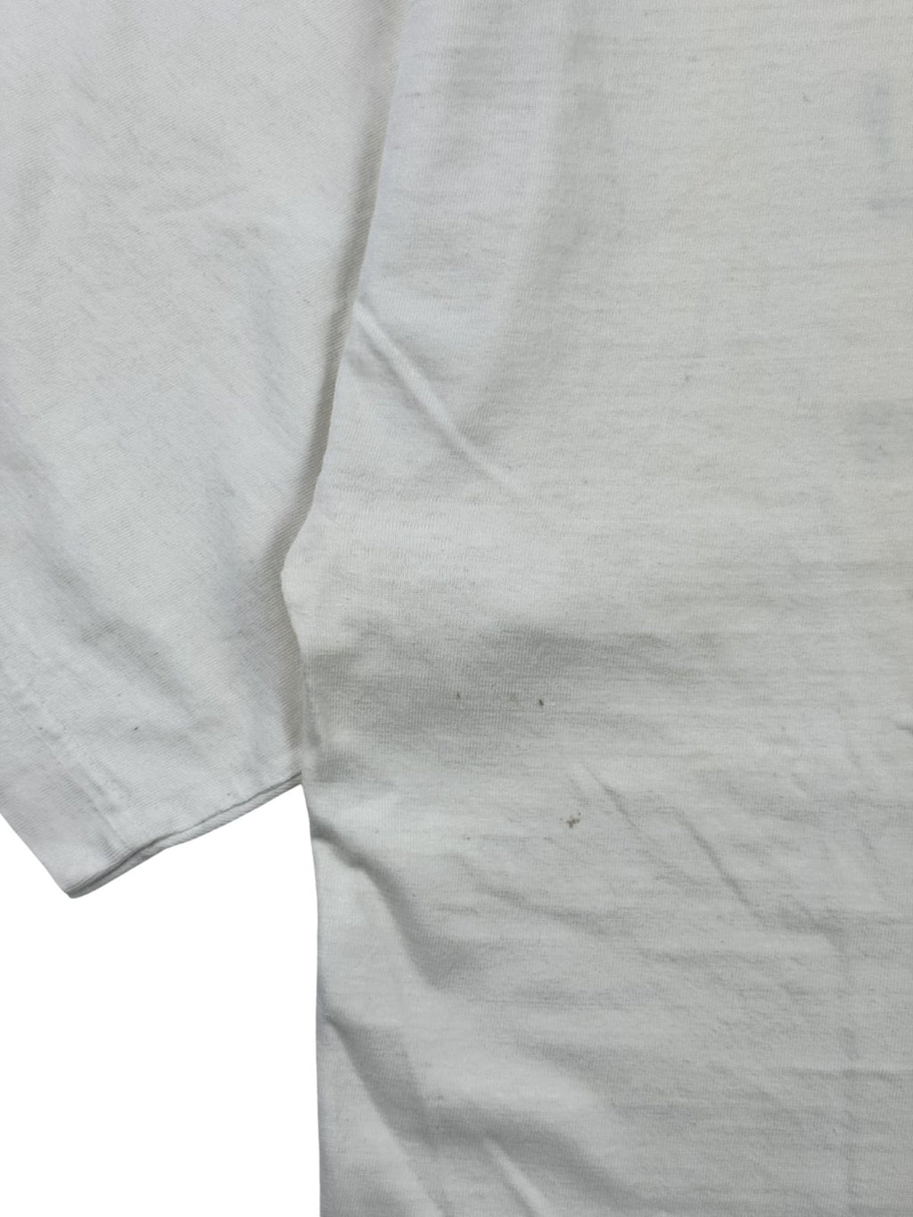 Detailaufnahme der linken Vorderseite eines weißen Vintage-Shirts zur Zustandsüberprüfung mit zwei kleinen, dunklen Flecken auf dem hellen Stoff nahe der Seitennaht.