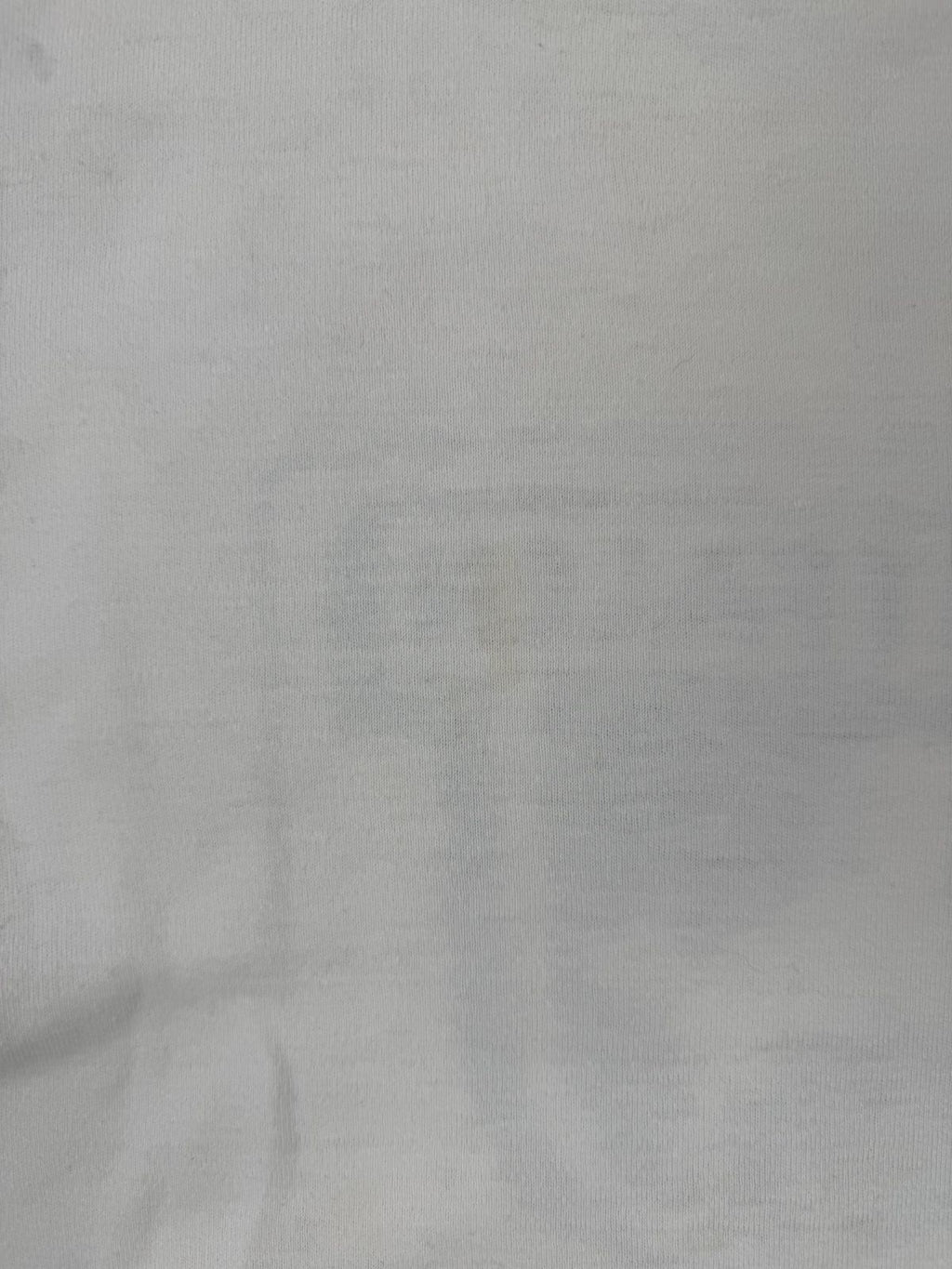 Makro-Ansicht der Stoffoberfläche; zeigt die authentische Textur des gealterten T-Shirts und eine kleine, unauffällige Verfärbung (True Vintage Condition).